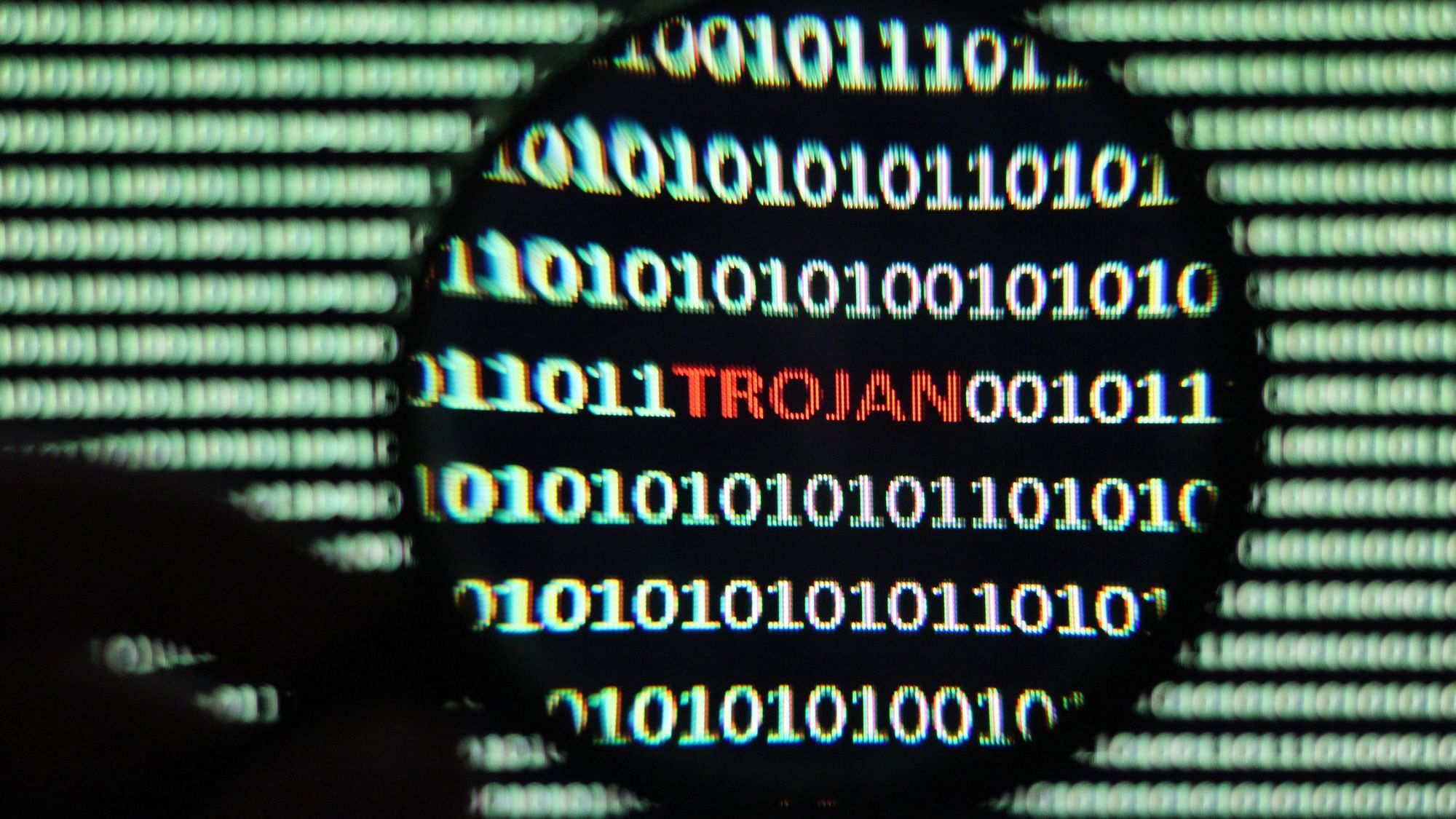 Binärer Code auf einem Bildschirm, ein Ausschnitt wird durch ene Lupe vergrößert. Wir sehen mehrere zeilen des Binärcodes in weiß und in rot dazwischen das Wort Trojan.