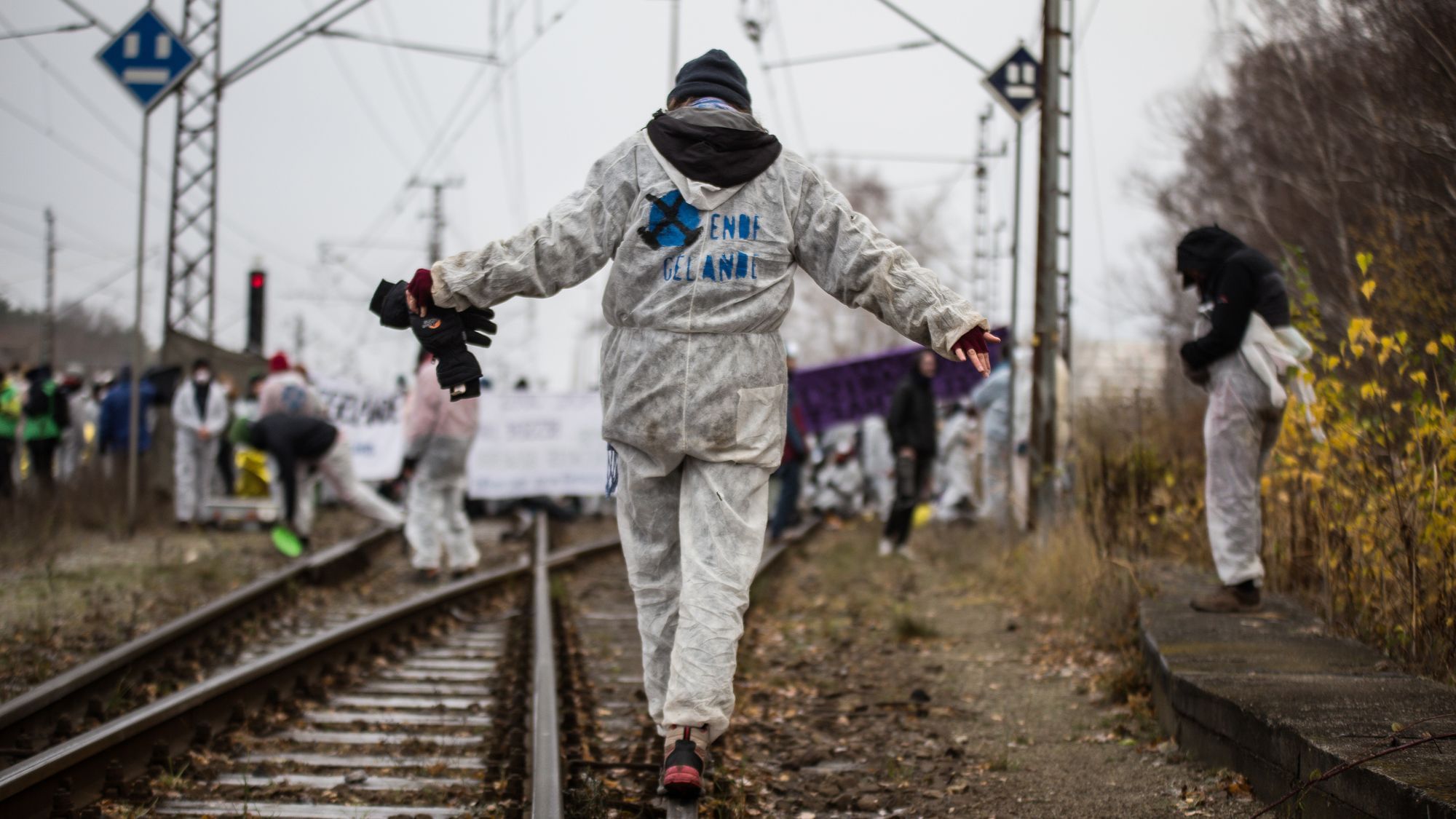 Eine Person in weißem Overall balanciert auf deinem Zuggleis welches Teil der Kohlenbahn für ein Braunkohlenkraftwerk ist. Auf dem Maleranzug ist der Begriff „Ende Gelände“ lesbar.