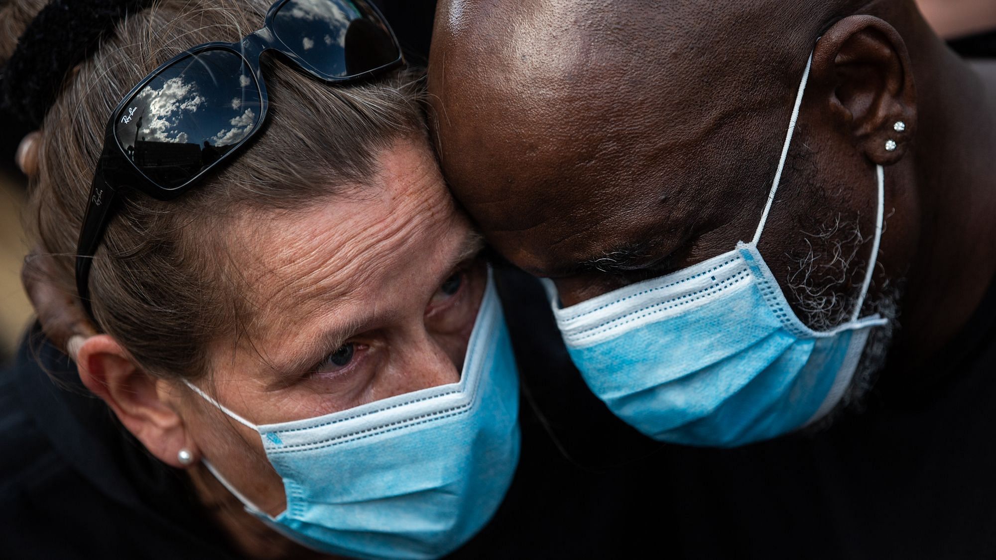 Wir sehen zwei Menschen, eine weiße weiblich gelesene und eine Person Of Color, die Kopf an Kopf zueinander stehen.
