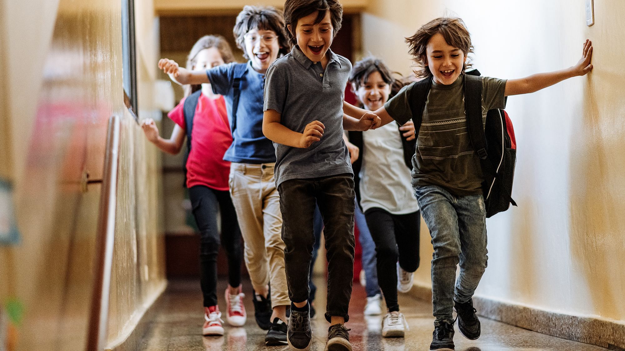 Mehrere Kinder rennen auf dem Gang einer Schule, sie lachen dabei. 