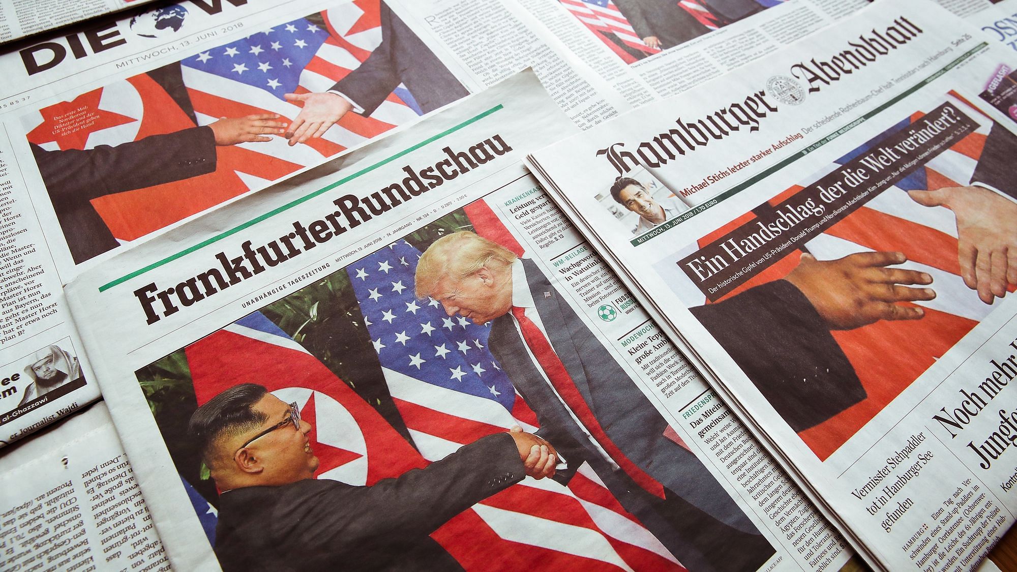 Wir sehen die Vorderseite von verscheidenen Zeitungen – auf allen ist ein Foto vom Trump und Kim jong un zu sehen, wie sie sich die Hand geben.