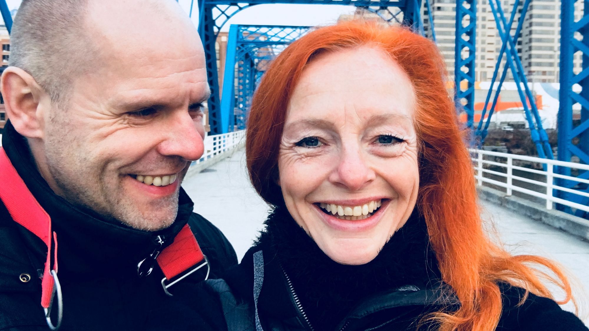 Wir sehen ein Frau mit rotgefärbten, langen Haaren, die in die Kamera schaut. Blaue Augen, ernster Blick.