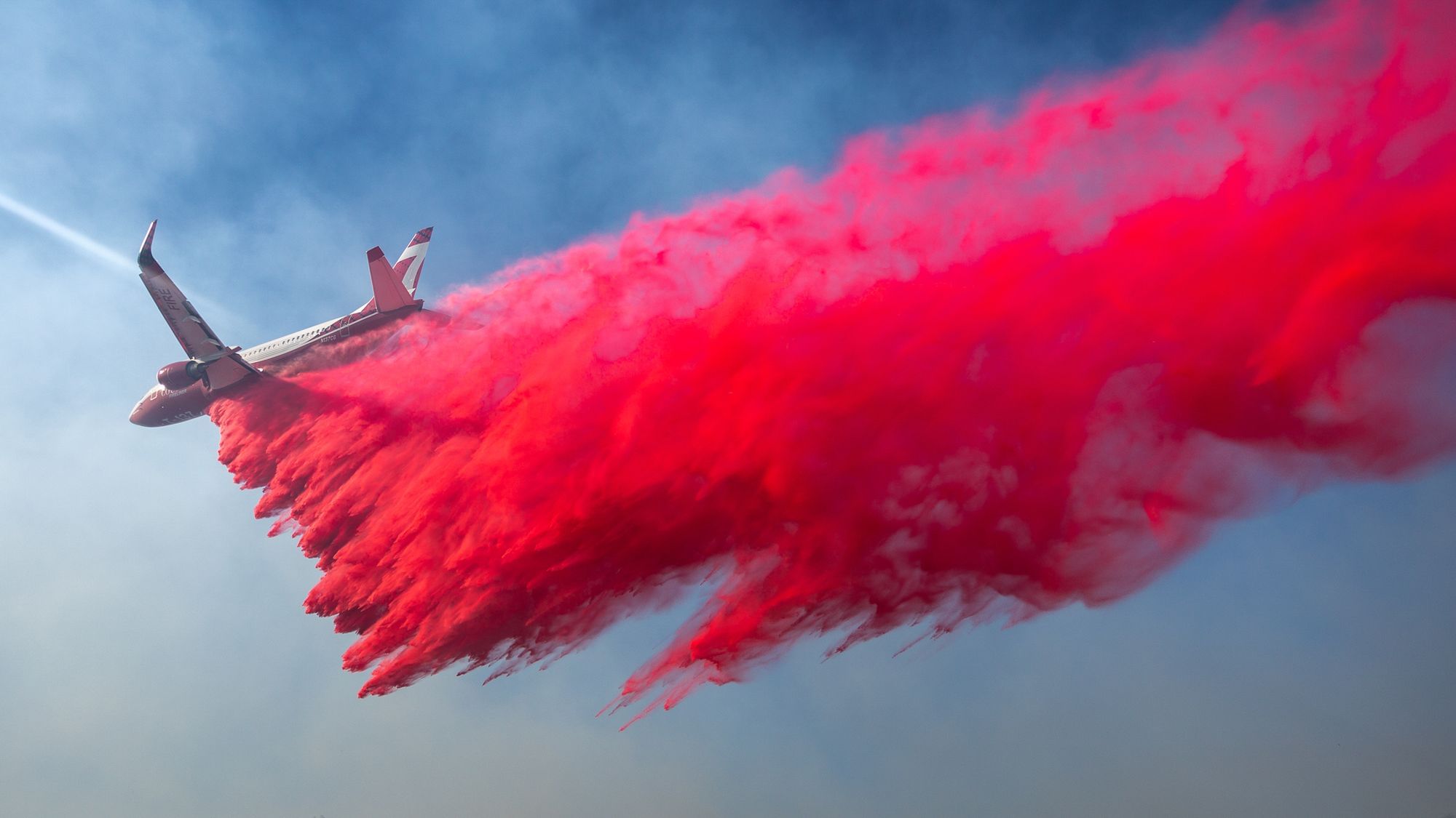 Wir sehen ein Flugzeug, das von oben einen Brand (den wir nicht sehen) löscht, indem es eine knallrote Flüssigkeit abwirft. 