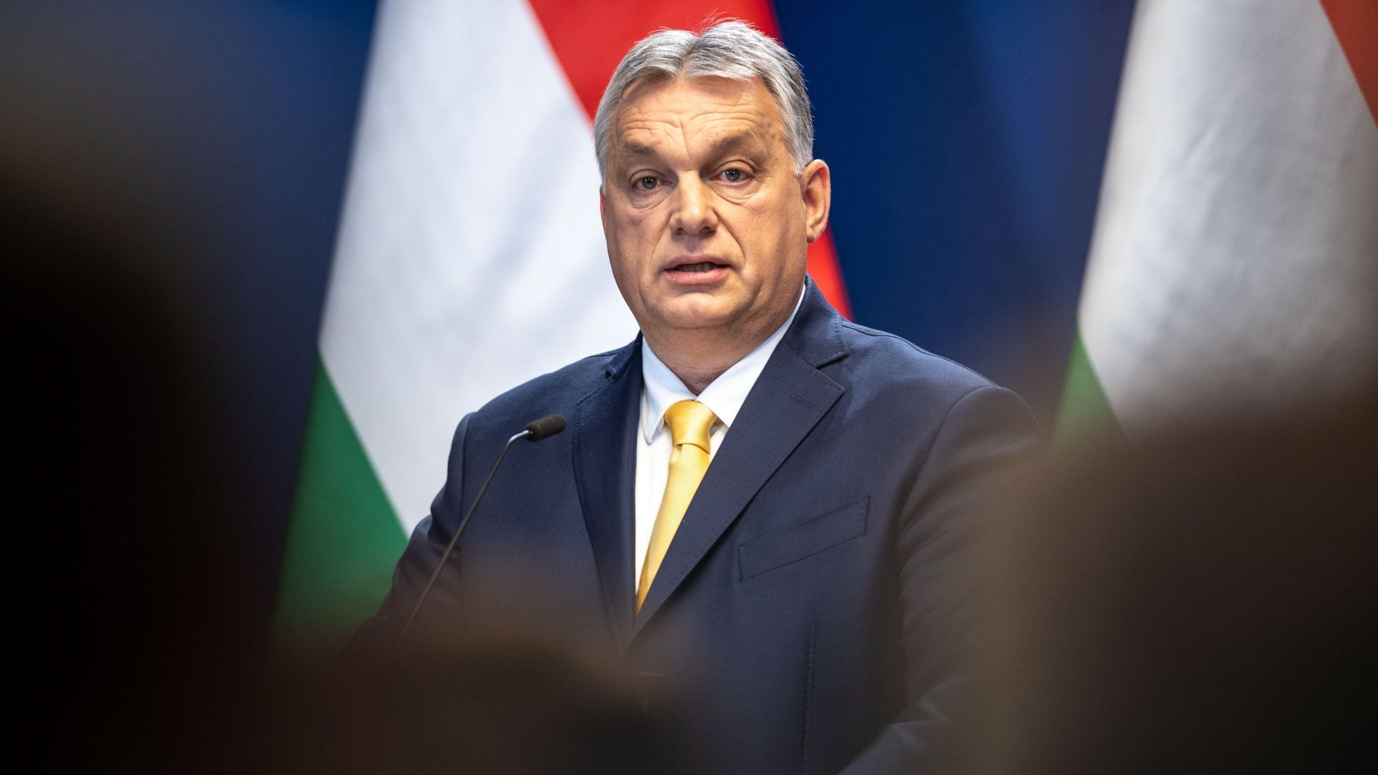 Wir sehen Victor Orban vor ungarischen Flaggen zu Menschen sprechen. 