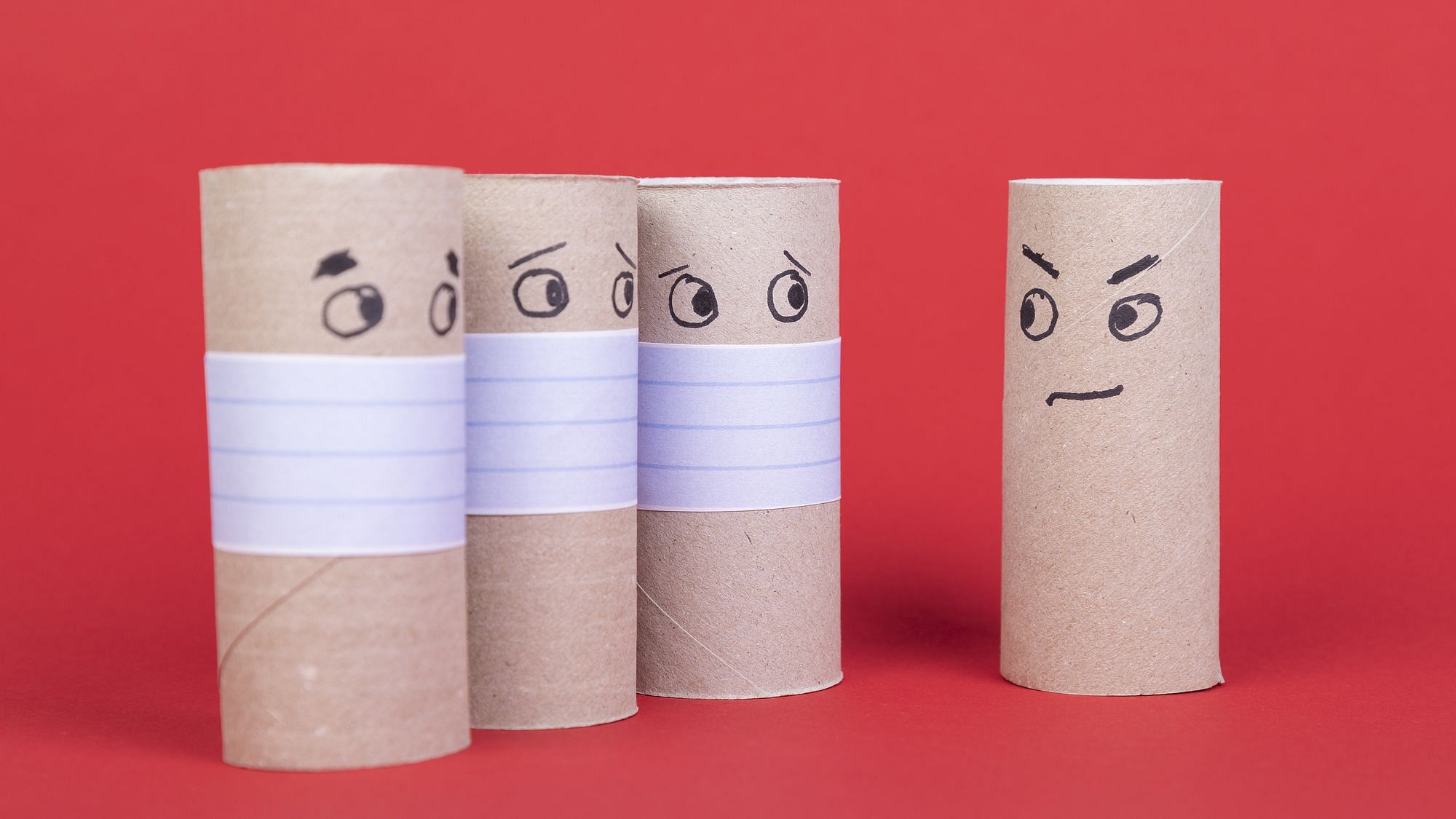 Vier leere Toilettenpapierrollen, drei mit Gesichtsmaske mit Blick auf eine ohne Mundschutz.