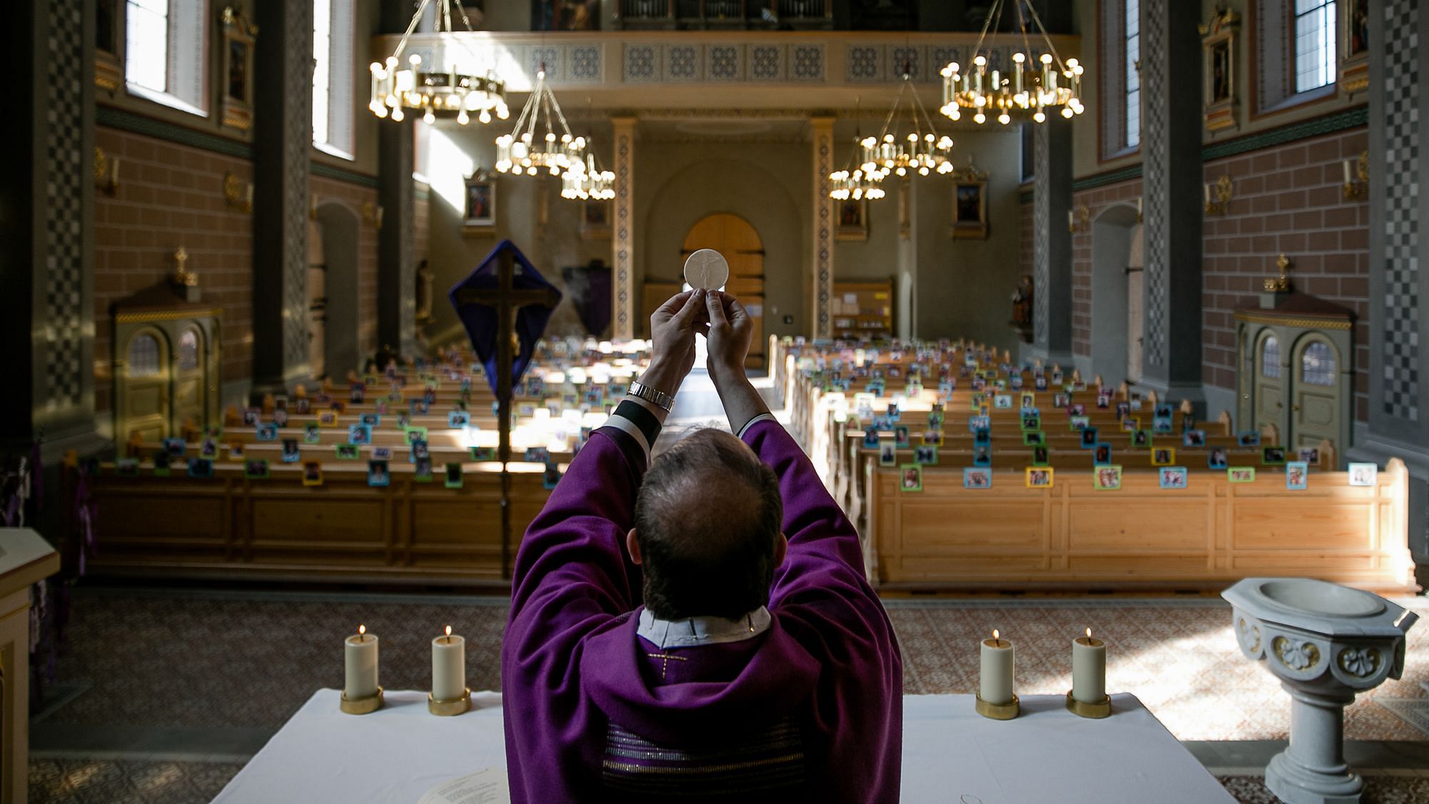 Ein Priester hält ein Hostie während der Wandlung vor einer leerer Kirche hoch während der Corona Krise.
