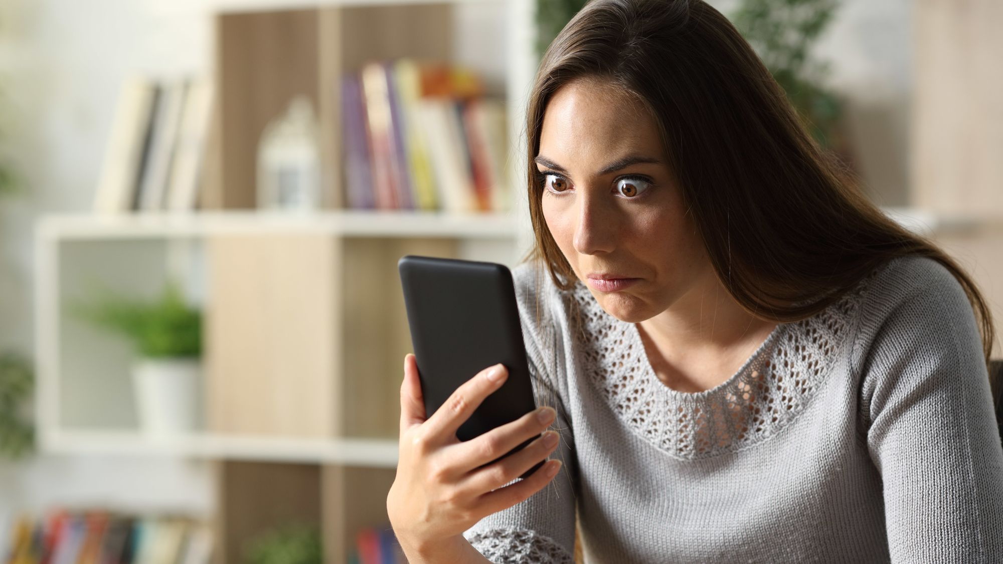 Verwirrte Frau schaut zu Hause überrascht aufs Telefon. 