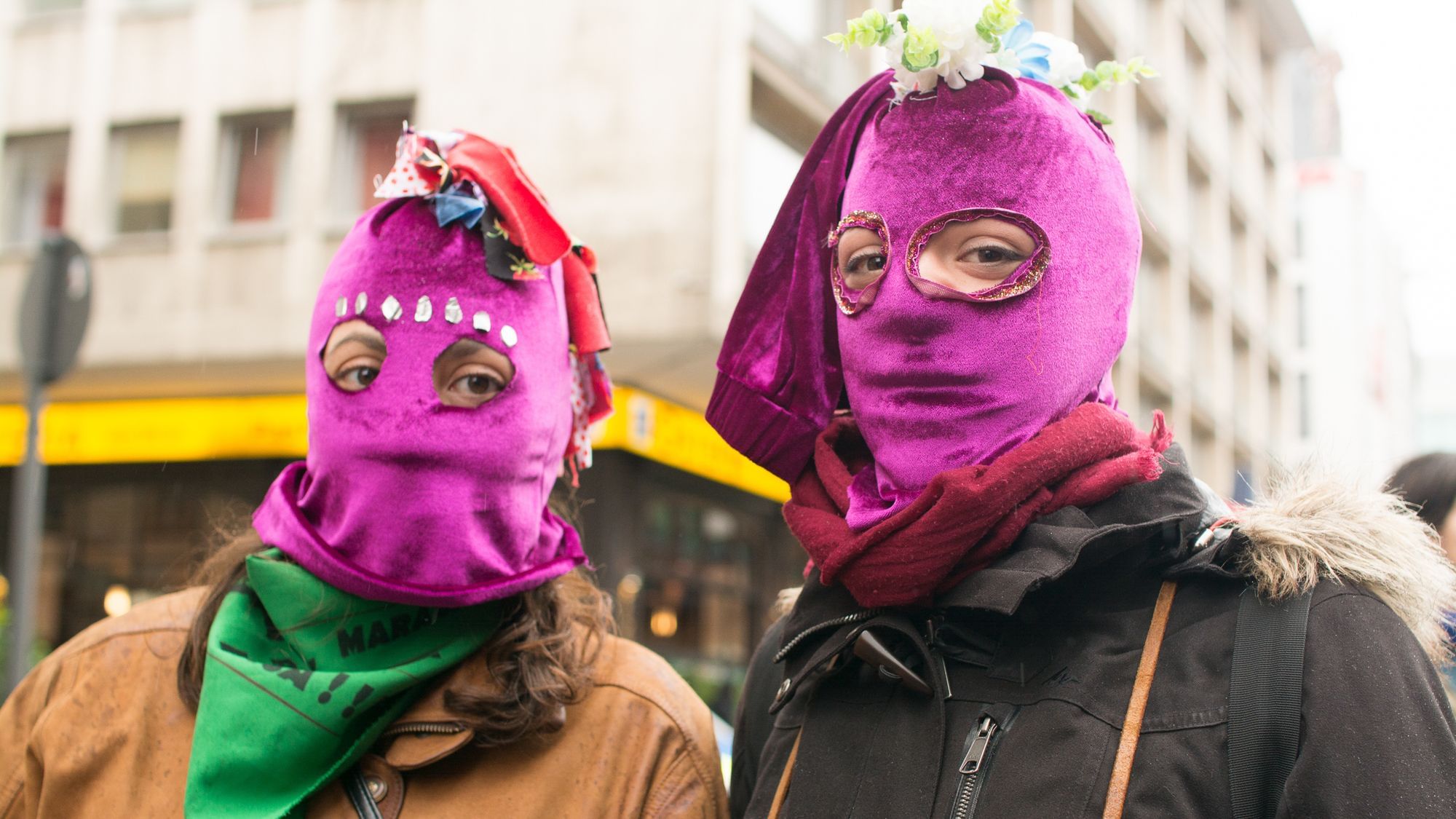 Zwei Menschen in lila Sturmhauben blicken skeptisch auf uns. 
