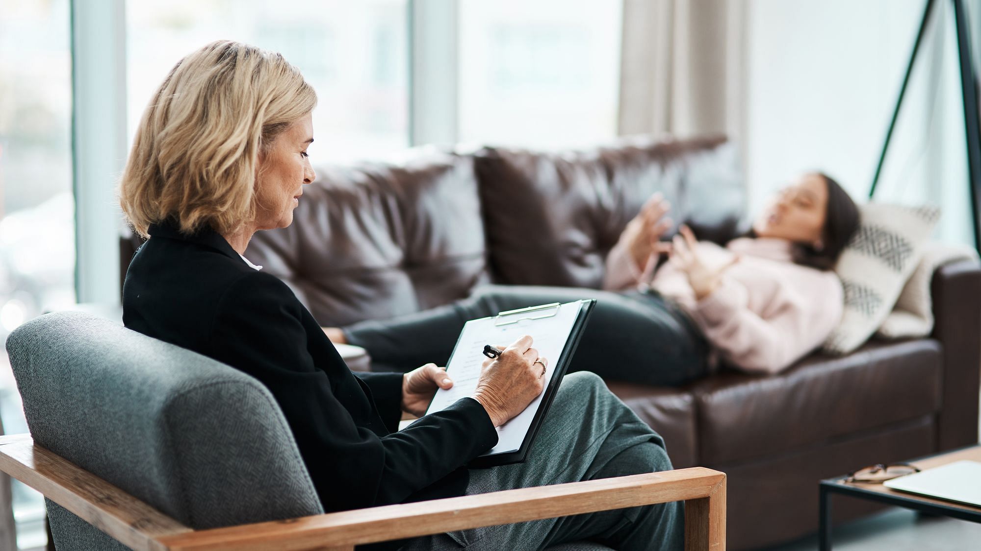 Eine Therapeutin macht sich Notizen während die Patientin auf dem Sofa liegt.