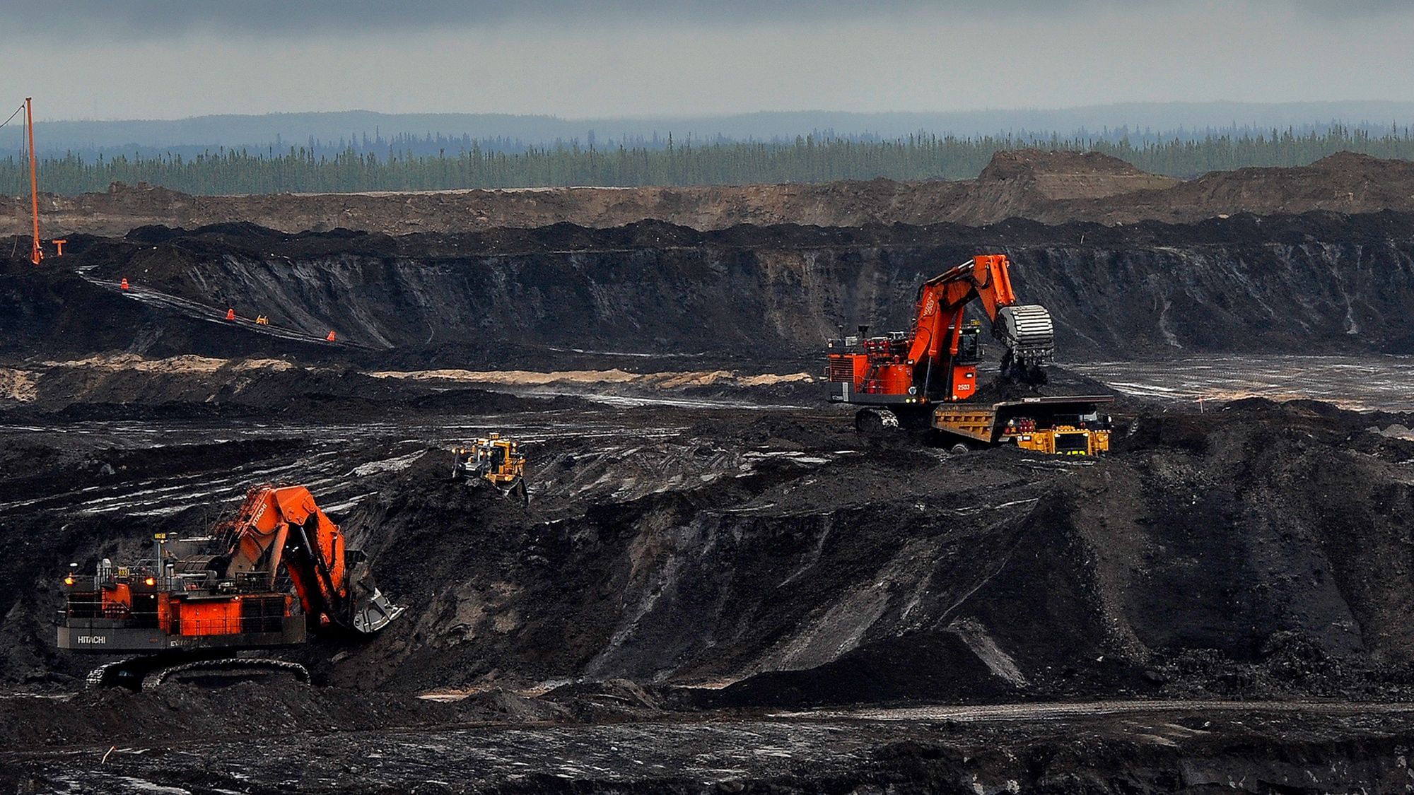 Zwei leuchtend rote Bagger in einer schwarzen Öl-Sand Mine in Kanada.