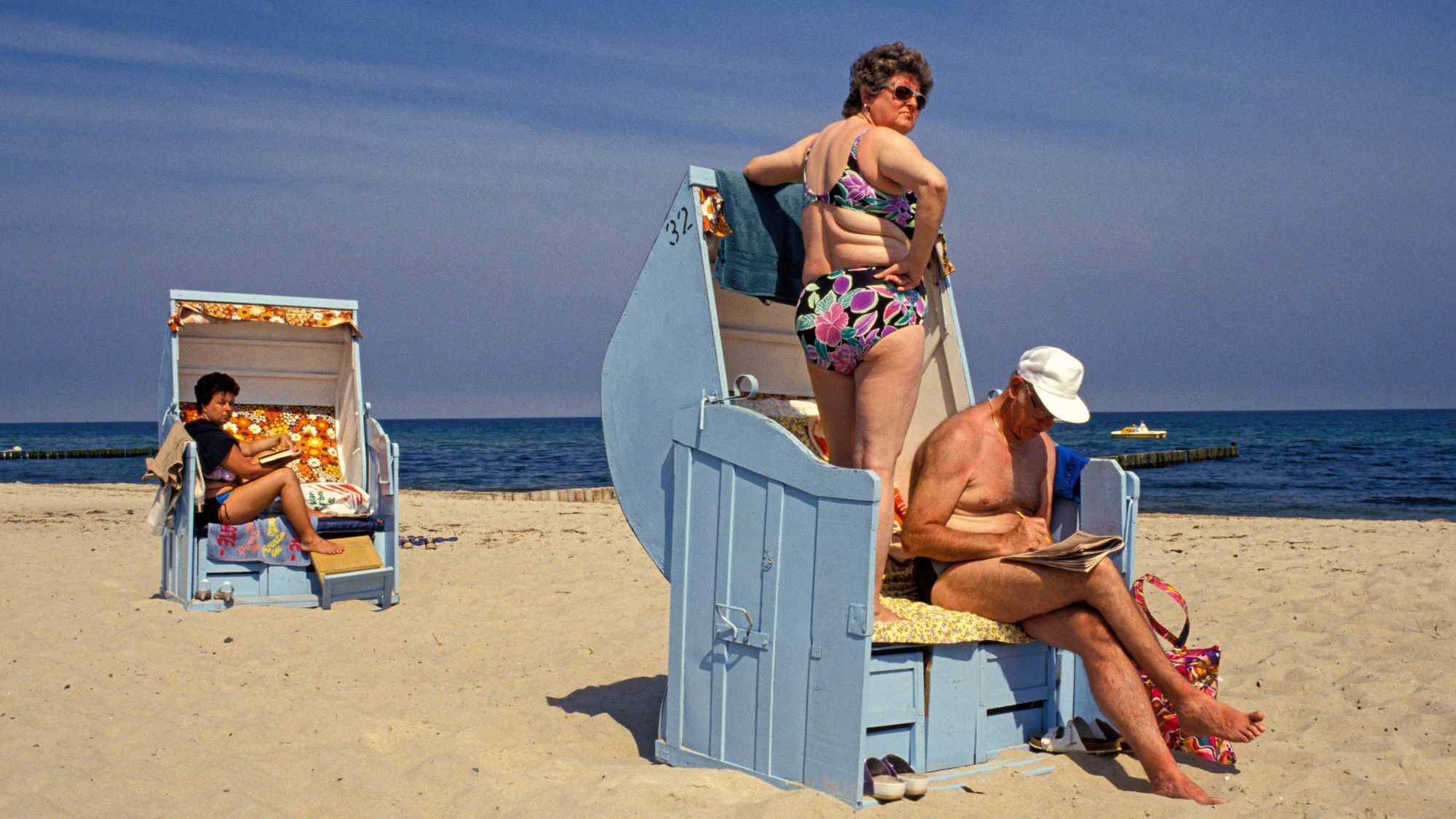 Eine Frau Steht auf ihrem Strandkorb und beäugt die Umgebung kritisch. Wir sehen das Meer hinter ihr.