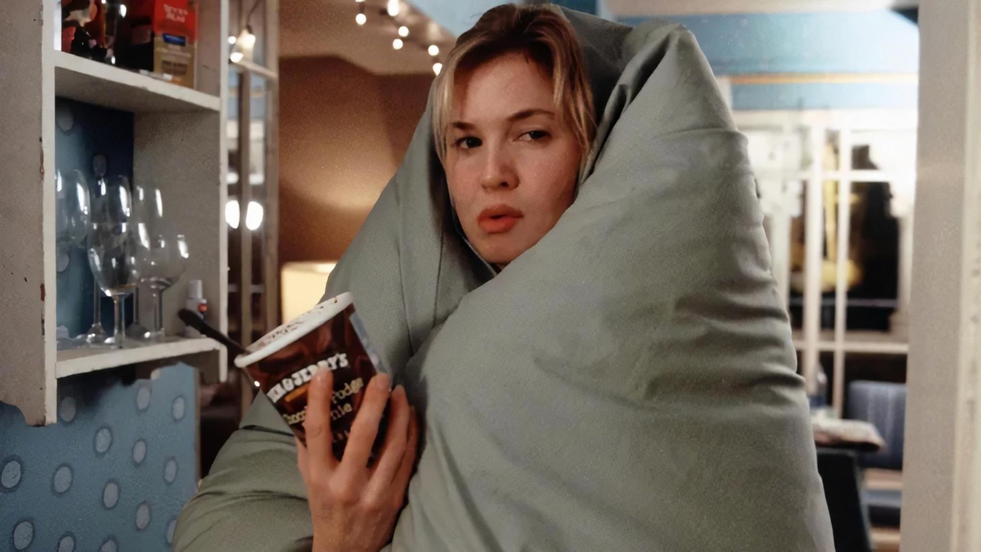 Ein Bild von Rene Zellweger als Bridget Jones, in eine Decke eingemummelt mit einer Pakcung Eiscreme.