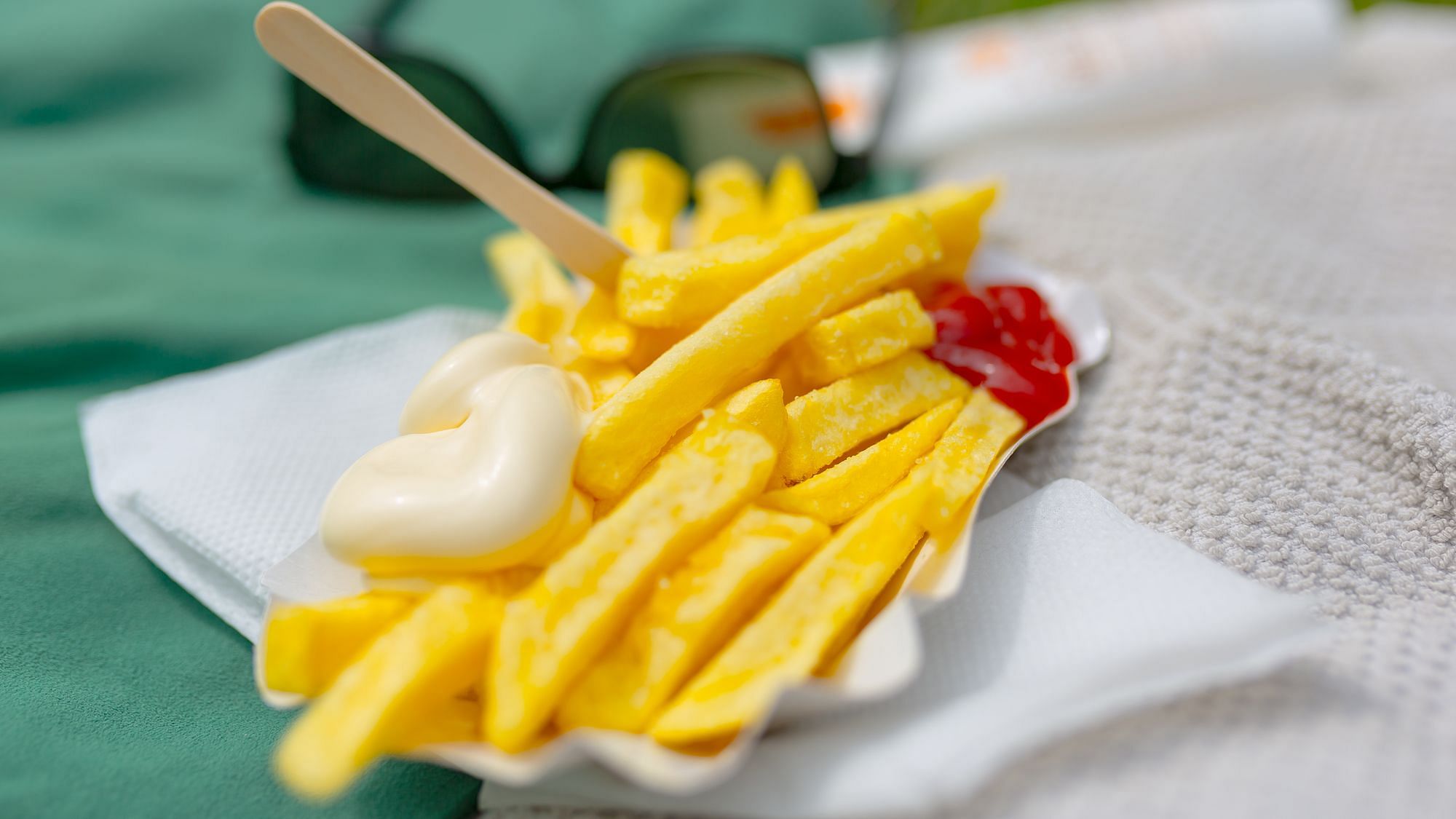 Ein Papierschiffchen Pommes mit Freibad im Hintergrund. 
