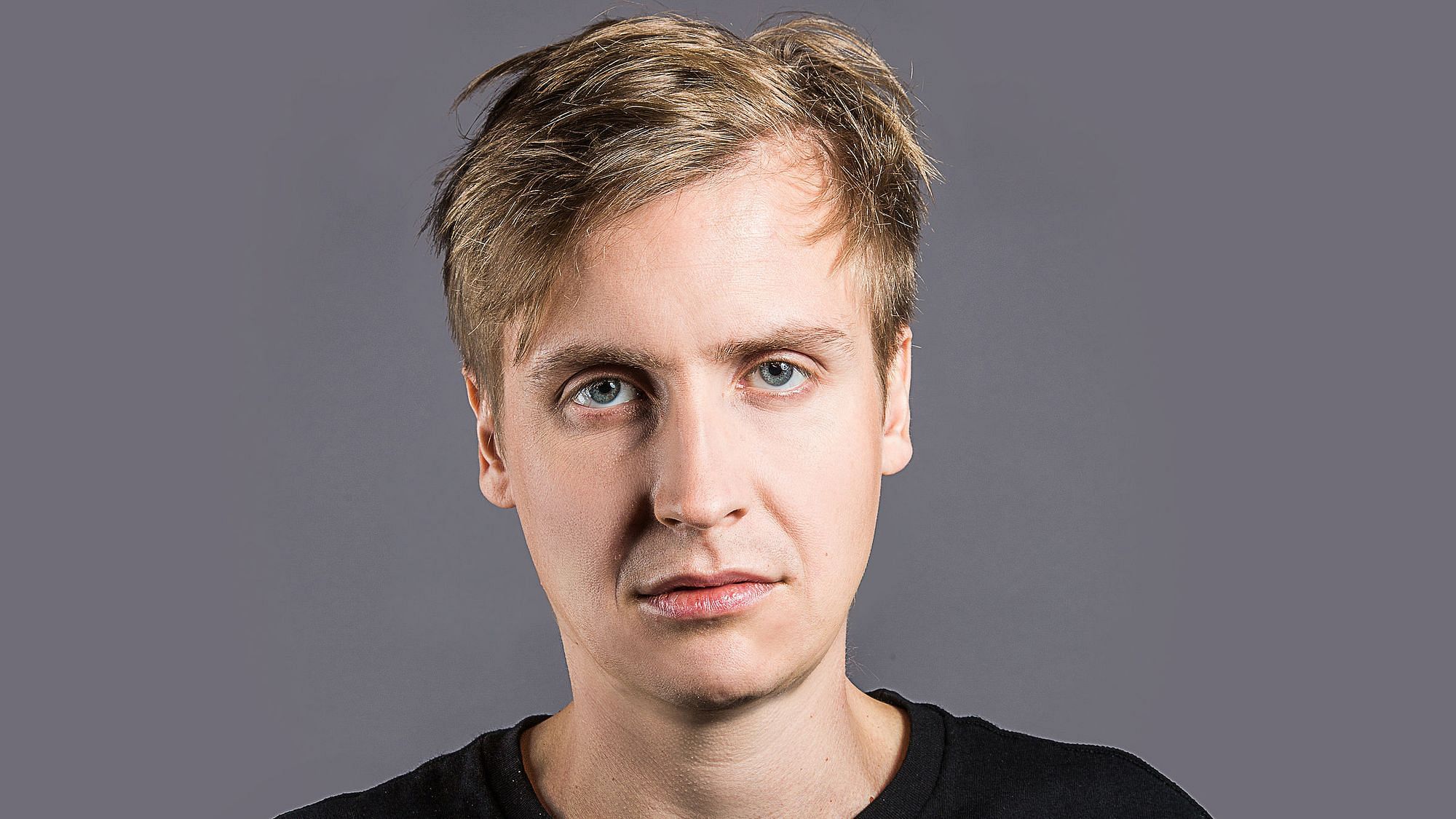 Till Reiners mürrisch dreinblickend, vor einem Anthrazitfarbenen Hintergrund