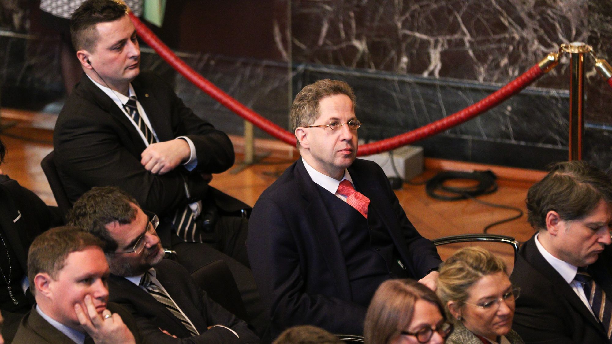 Hans-Georg Maaßen sitzt isoliert in einem Publikum. Die Menschen um ihm herum scheinen ihn eher zu meiden.