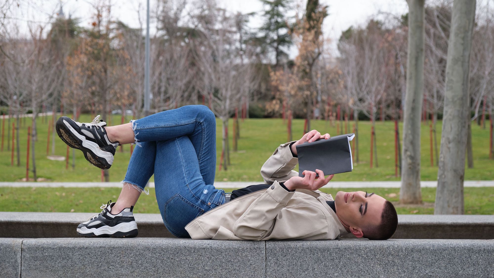 Eine androgyn, nicht-binär gelesene Person liegt auf einer Mauer, in ein Buch vertieft lesend.