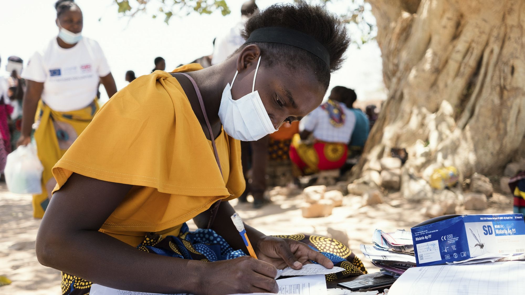 Eine Frau beugt sich über Gesundheitsdokumente, ihr Gesicht ist halb von einer Maske bedeckt.