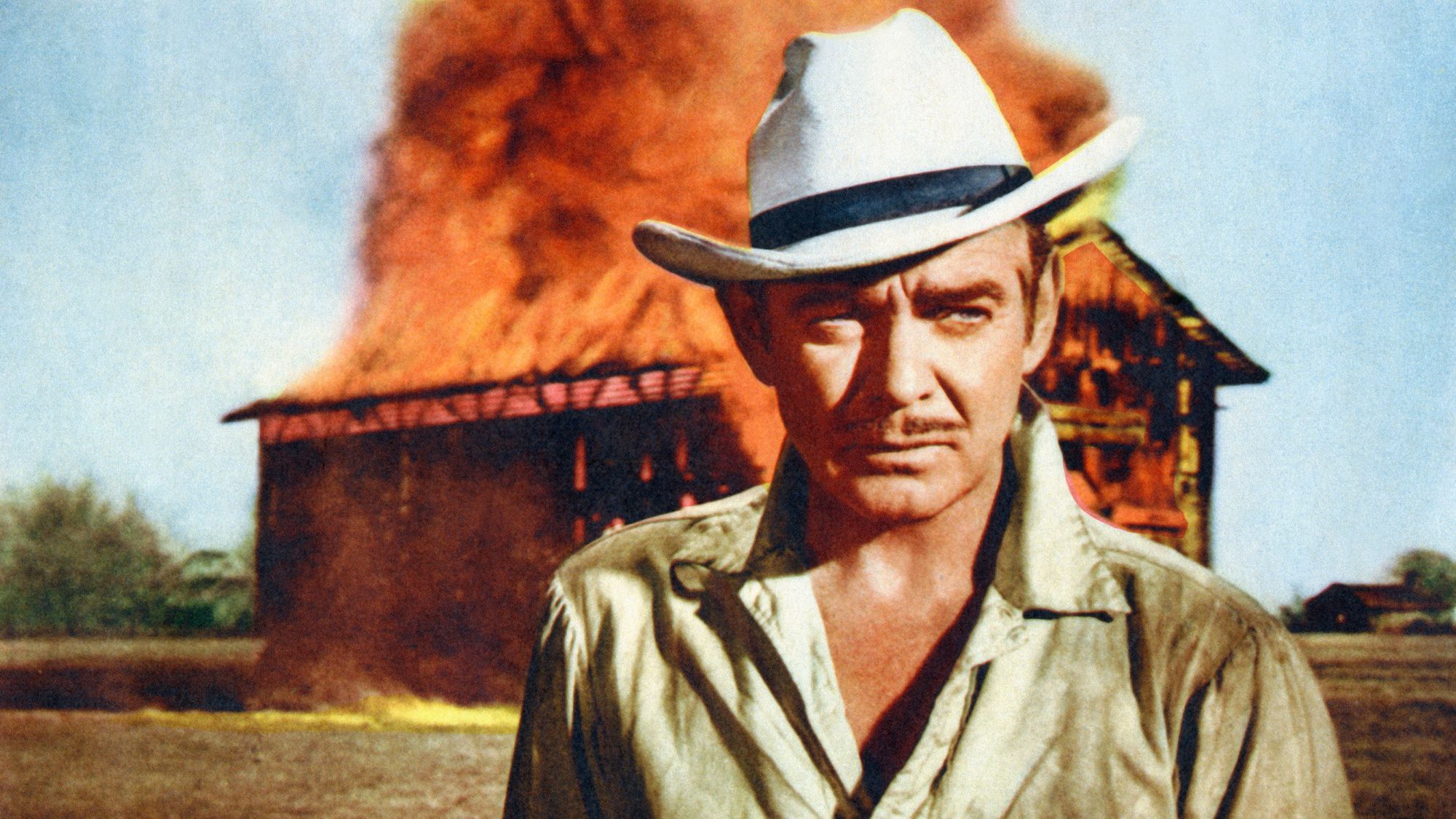 Clark Gable steht mit einem ernsten Gesicht vor einer brennenden Scheuen.