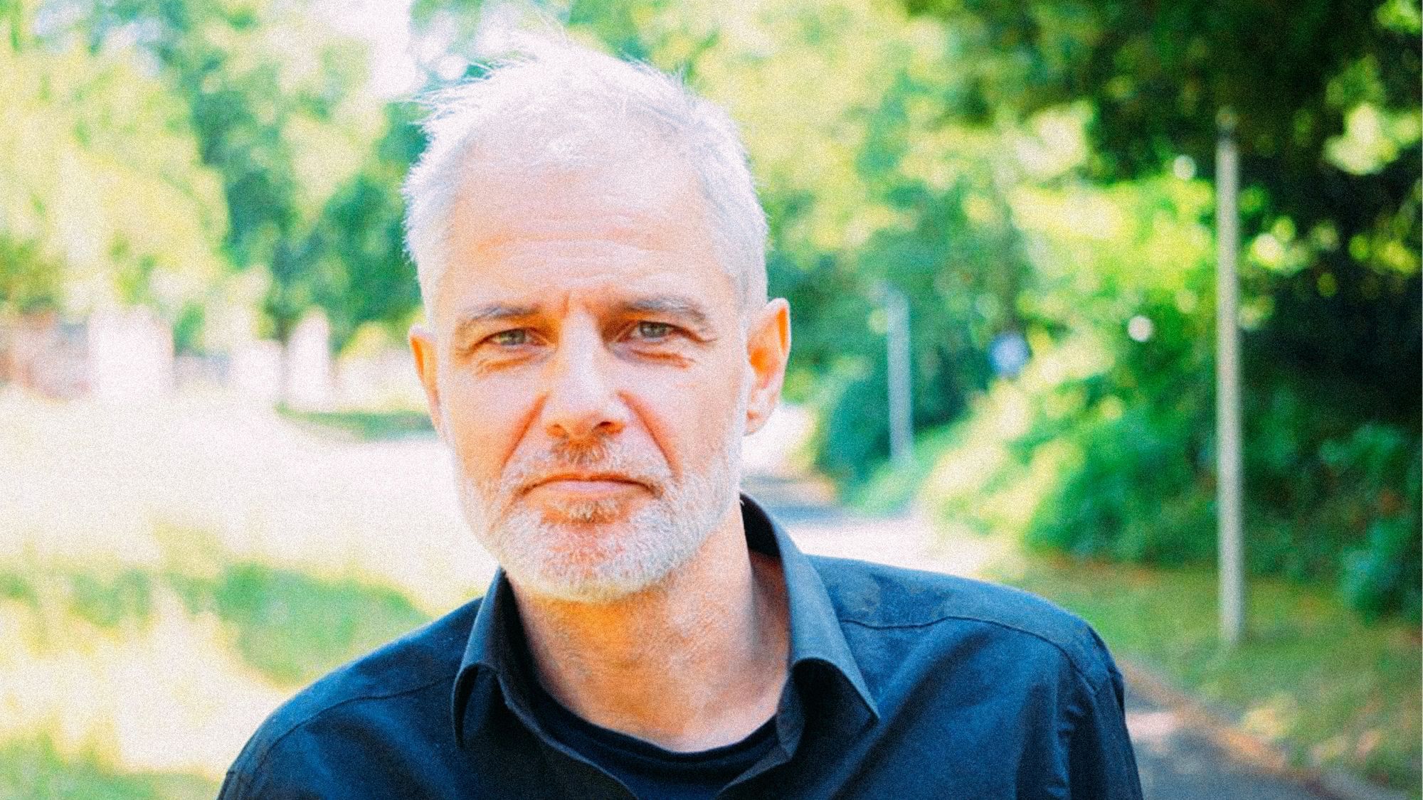 Ein Mann mit grauen Haaren vor grünem Hintergrund. 