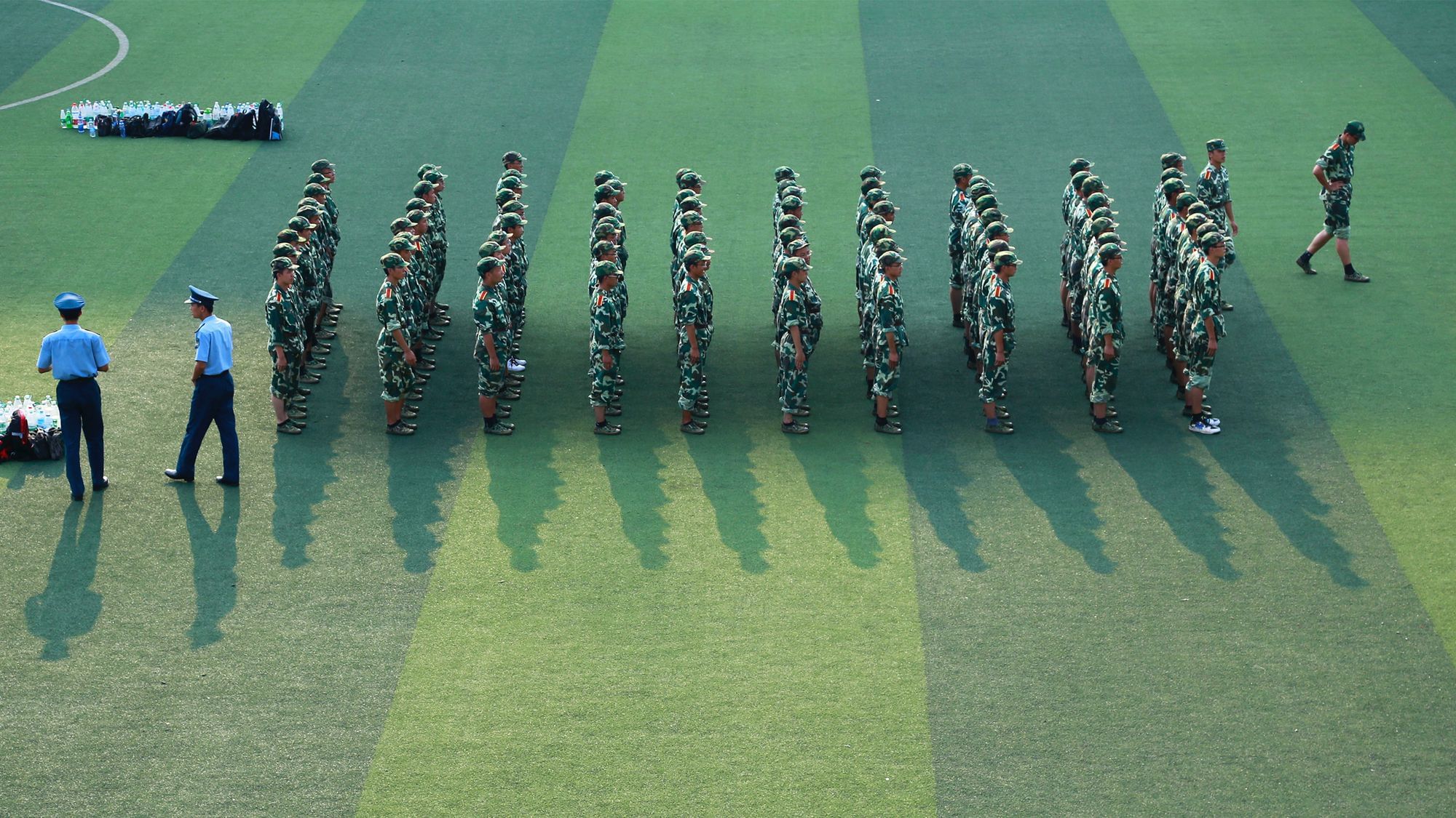 Junge Männer stehen früh morgens in Reih und Glied auf einem Footballfeld. Sie tragen Militäruniformen. 