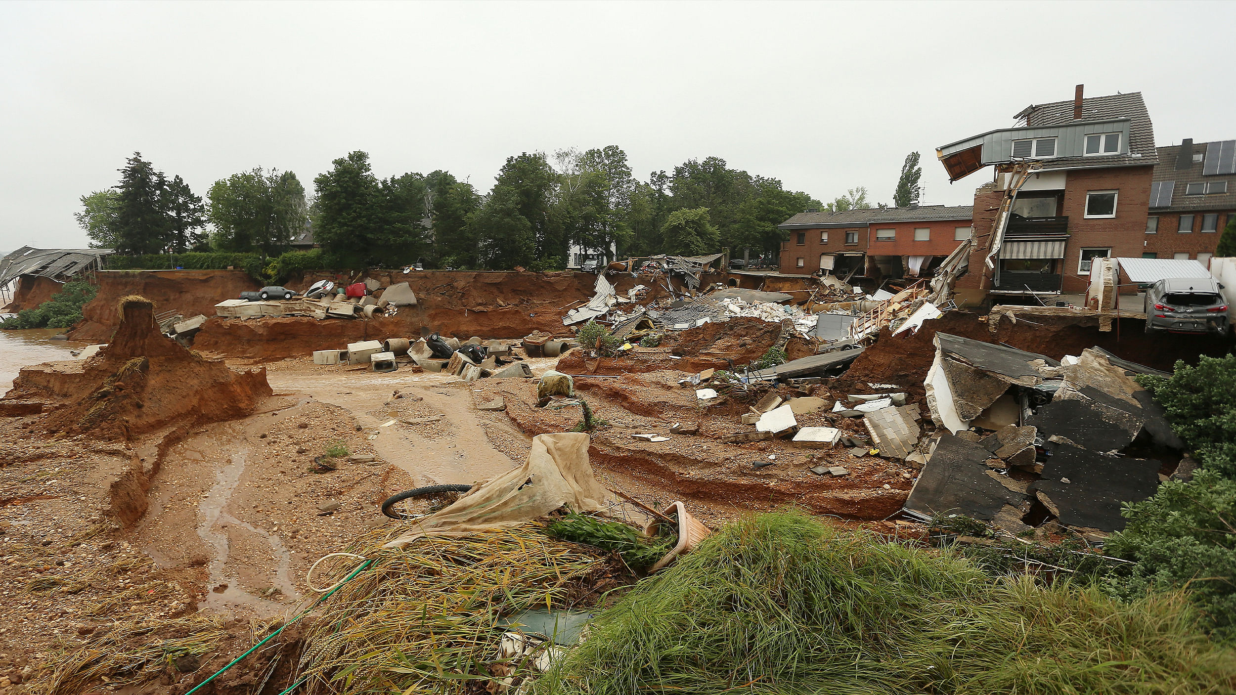Eine Szene aus dem Ahrtal von vor einem Jahr. Durch die Flut gab es einen Erdrutsch, rechts im Bild sieht man die Trümmer eines betroffenen Hauses. In der Ferne sieht man mehrere Autos, die abgerutscht sind.