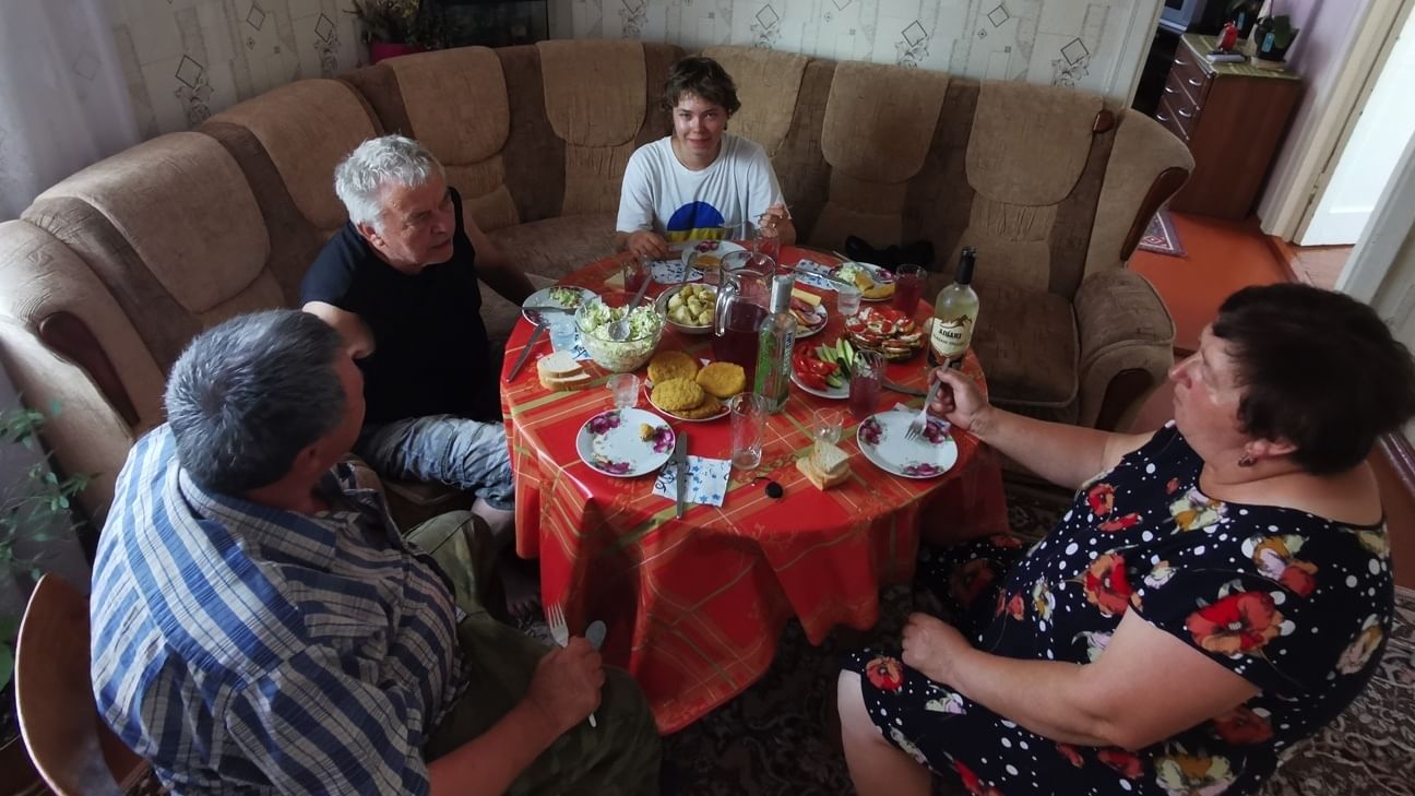 Vier Menschen sitzen um einen reich gedeckten Tisch. Sie sitzen auf einem altmodischen Ecksofa.