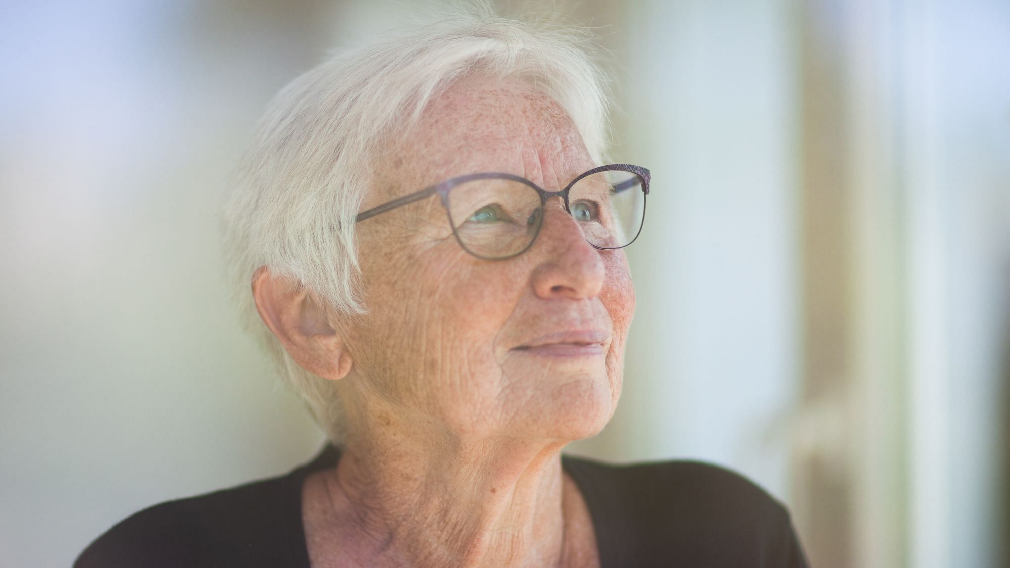 Wir sehen eine Nahaufnahme einer Frau mit grauen Haaren, die in die Ferne sieht.