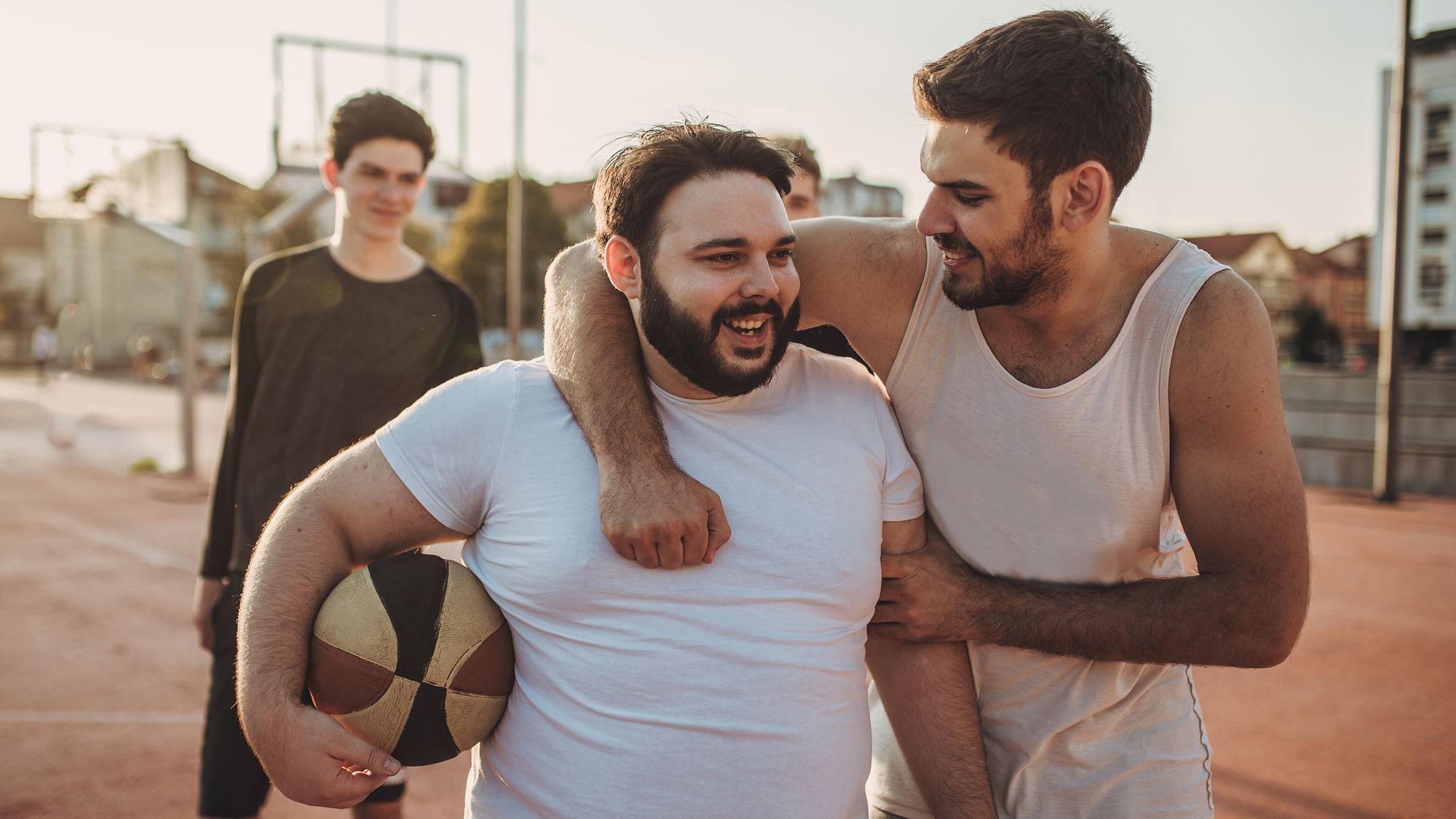 Wir sehen zwei Männer, die sich gegenseitig mit Basketball in der Hand necken – in der Mitte eine Person mit Übergewicht
