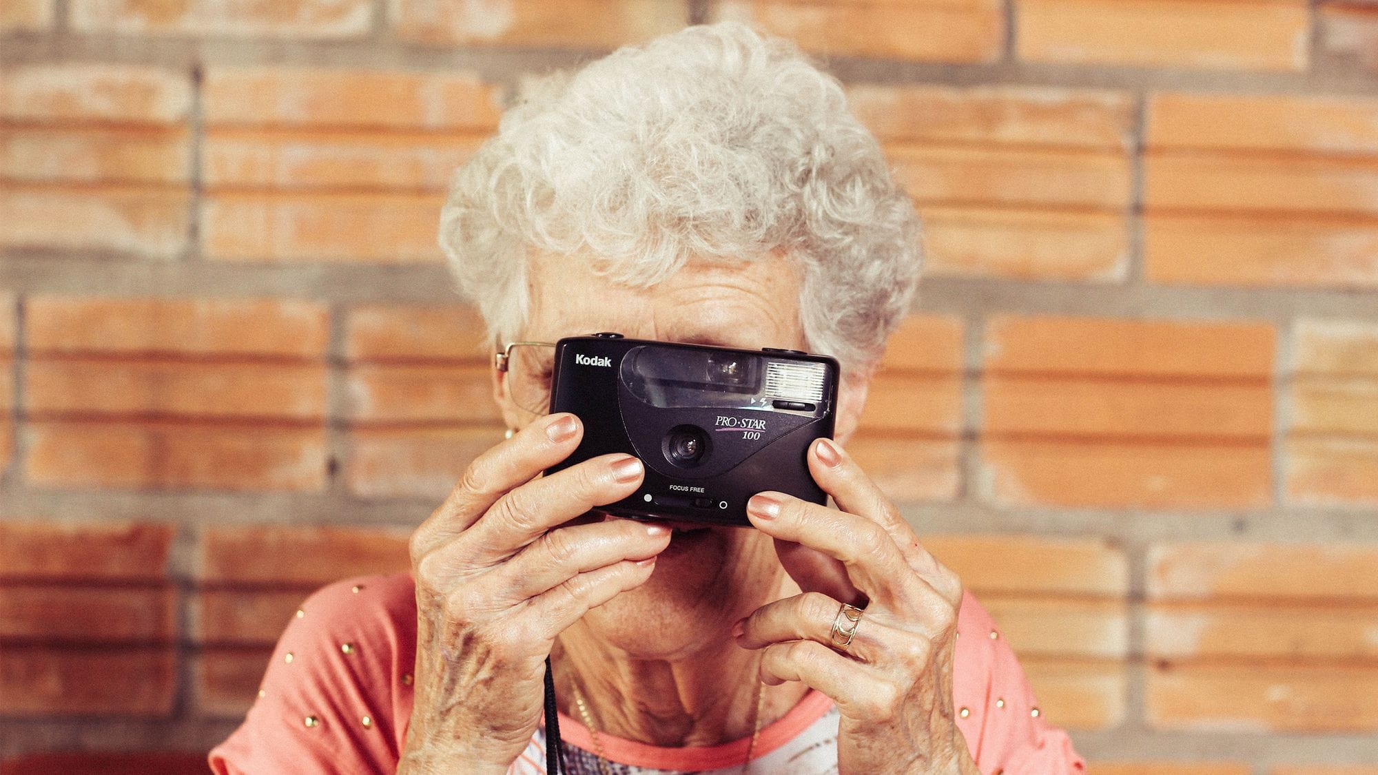 Eine Frau mit weißen Haaren hält sich eine Kamera vor das Gesicht. 