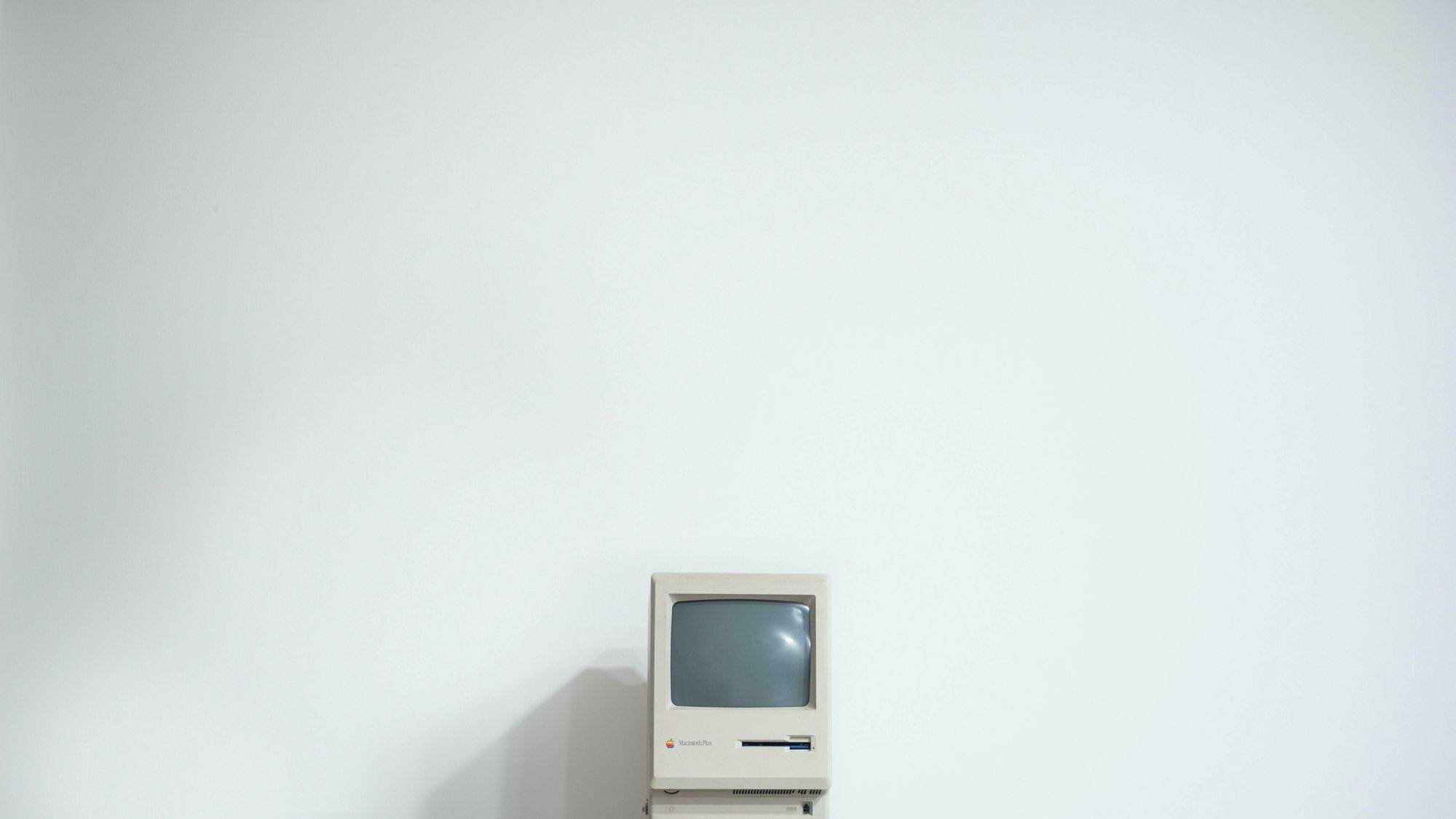 Wir sehen einen alten Apple aus den Achtzigern vor einer weißen Wand