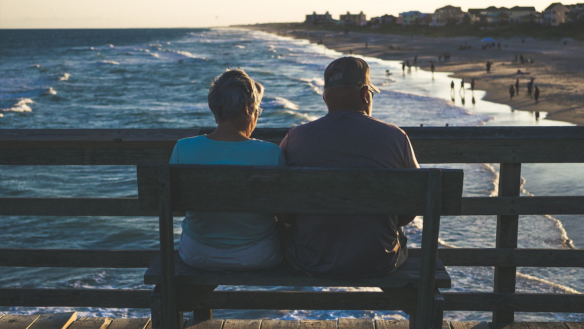 Zwei Menschen sitzen auf einer Bank und blicken auf das Meer und den Strand.