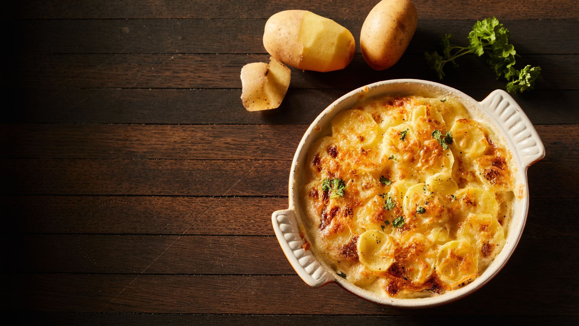 Ein Kartoffelgratin steht auf einem dunkelbraunen Tisch. 
