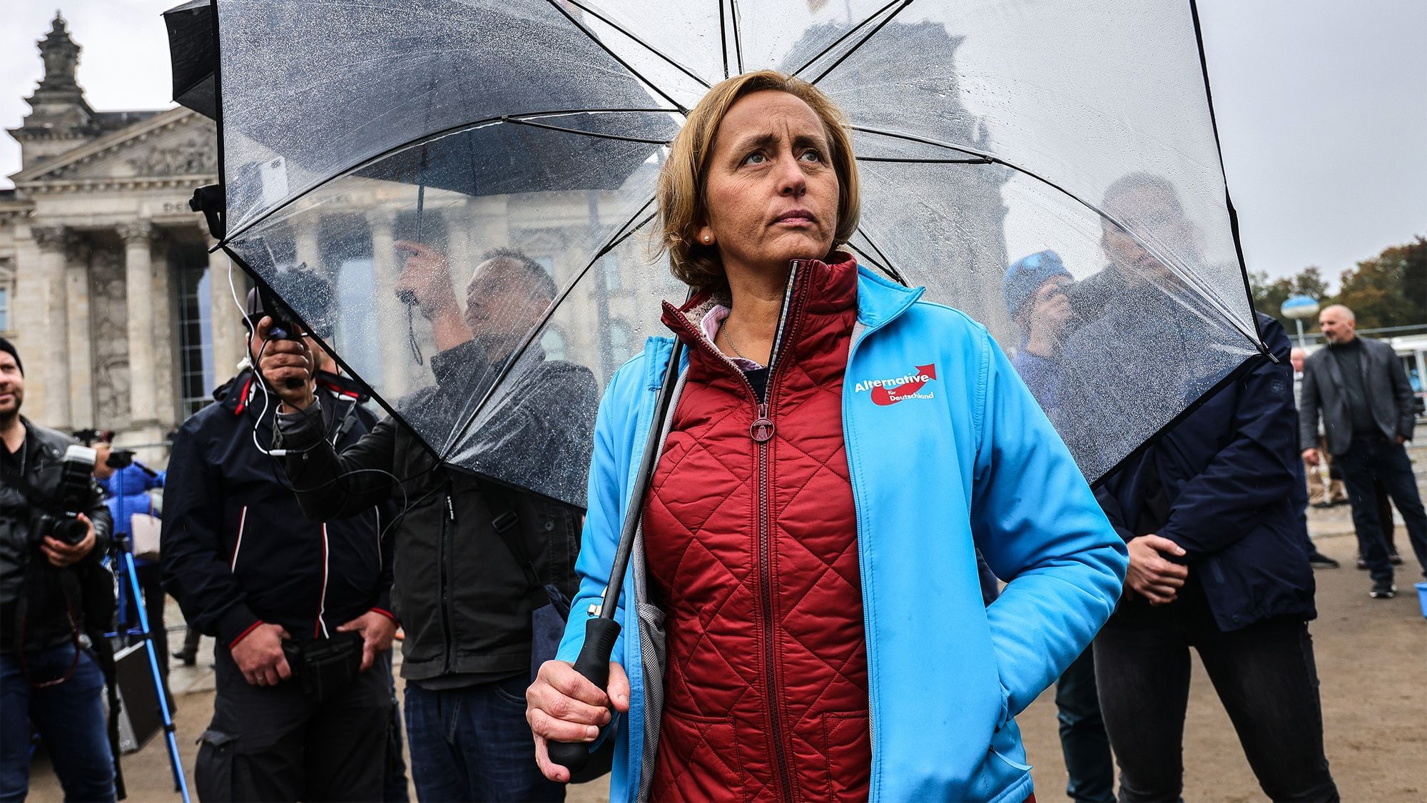 Beatrix von Storch unter einem Regenschirm. Sie trägt eine hellblaue Jacke mit dem Logo der AfD darauf.