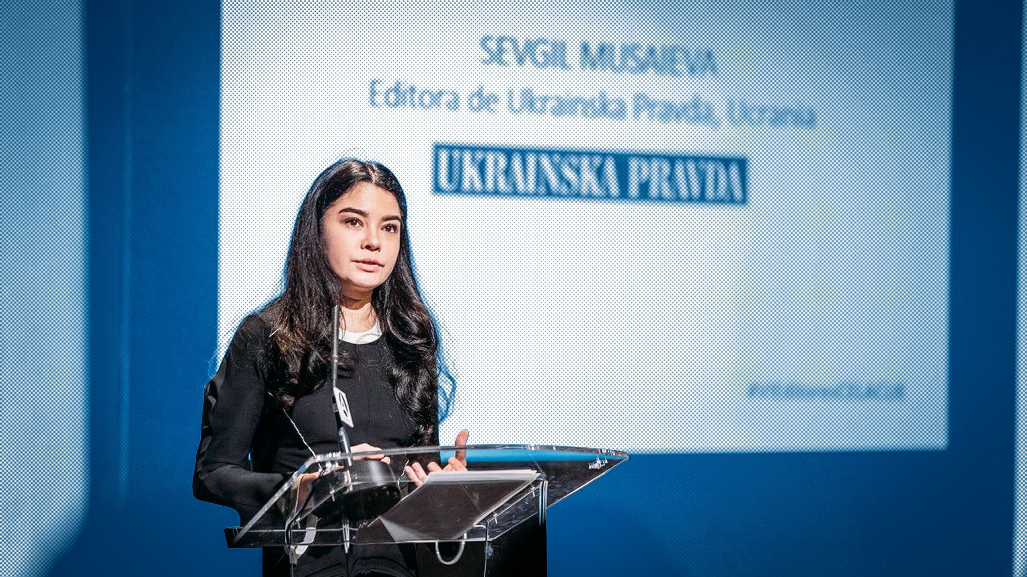 Die Journalistin Sevgil Musaieva steht an einem Pult und hält eine Rede. Hinter ihr an der Wand ist eine Power Point Präsentation mit der Überschrift „Ukrainska Prawda“.