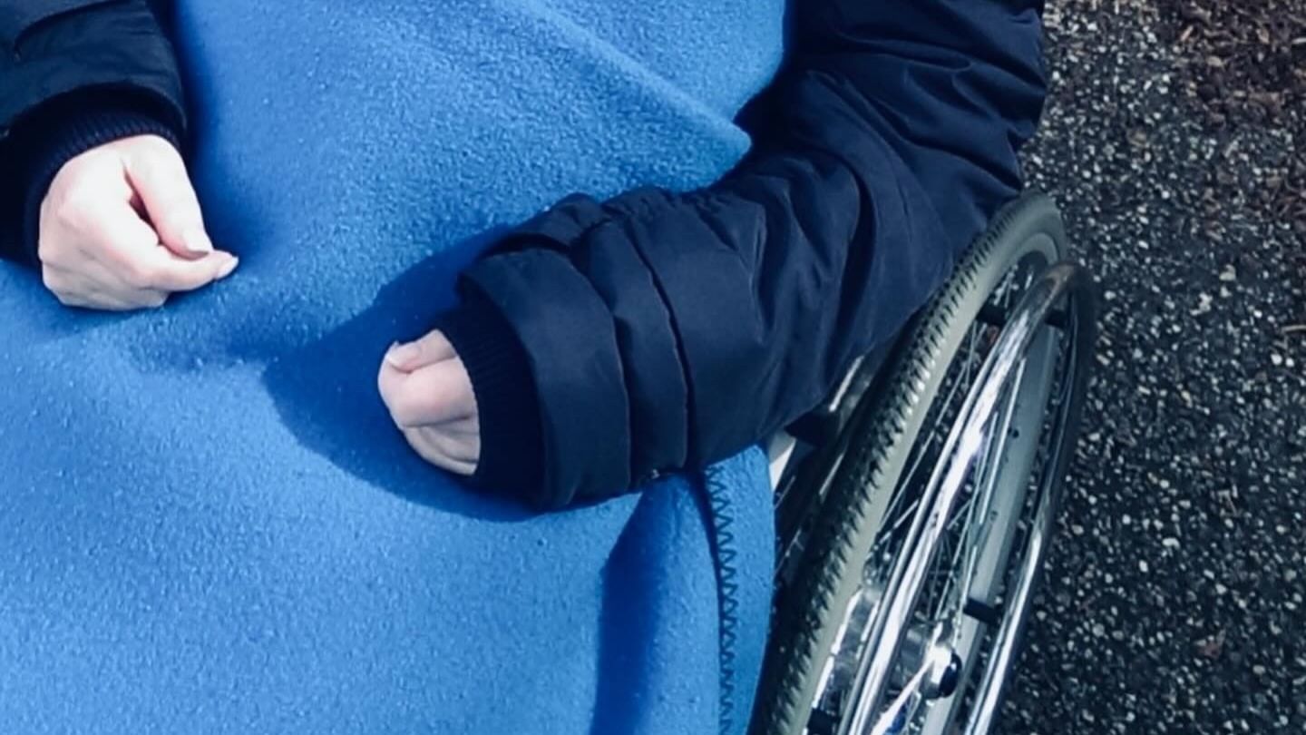 Eine Frau sitzt im Rollstuhl und hat eine blaue Decke auf dem Schoß.