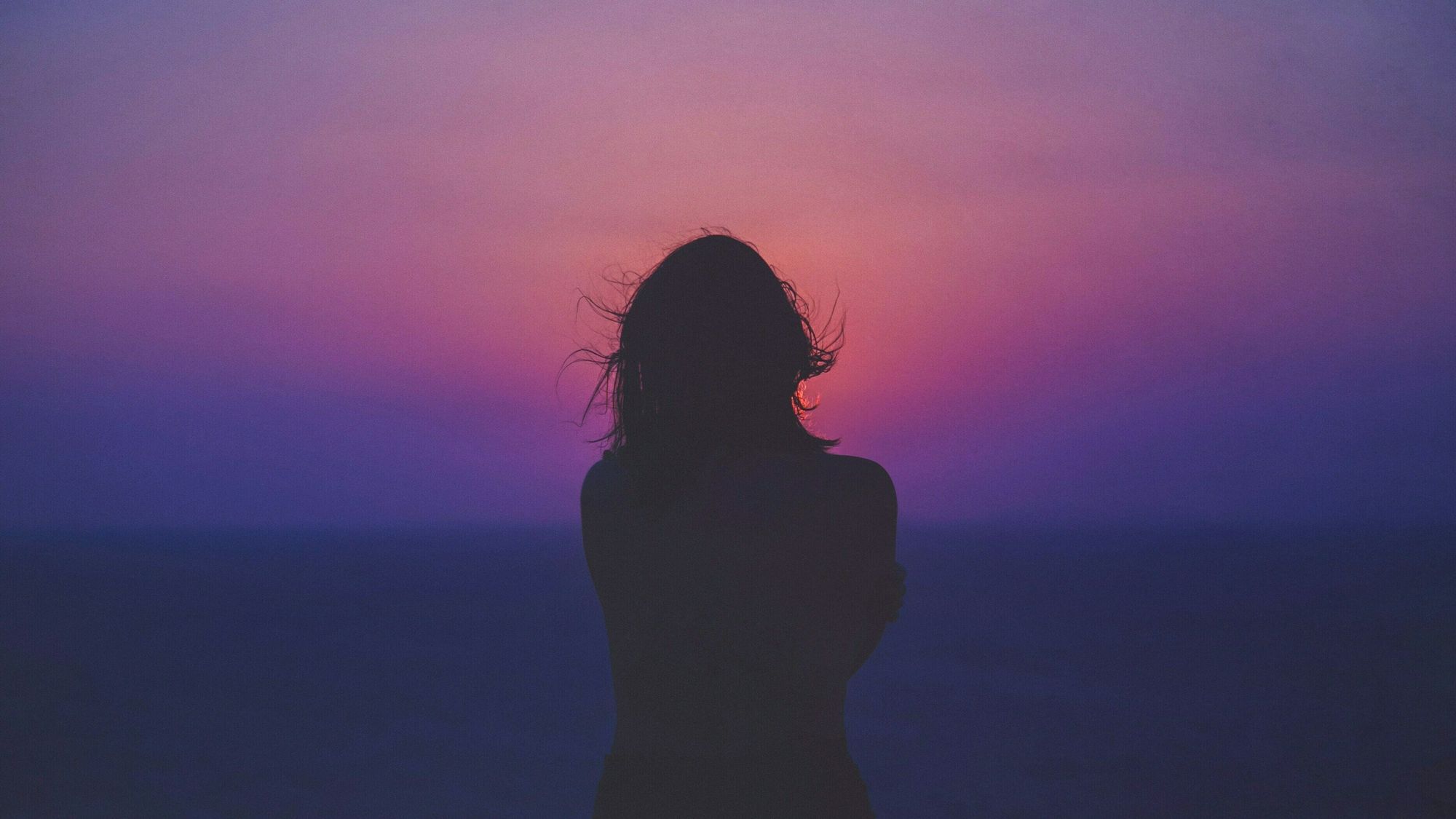 Eine Frau blickt alleine in den Sonnenuntergang.