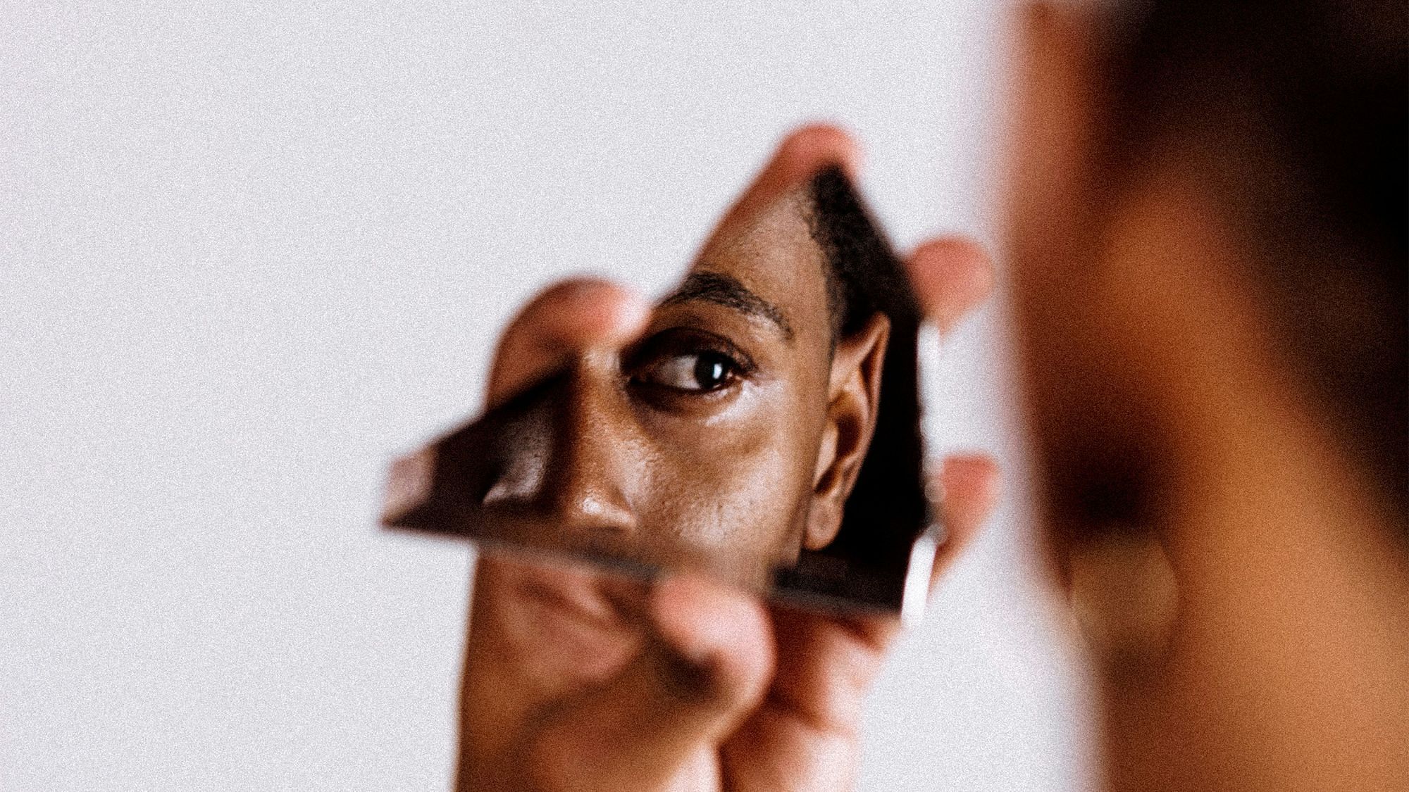 Ein schwarzer Mann hält eine Spiegelscherbe, sein Gesicht spiegelt sich teilweise darin.