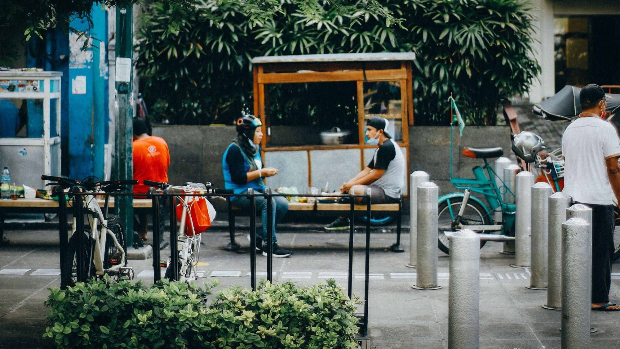 Zwei Menschen sitzen sich auf einer Bank gegenüber und unterhalten sich. Um sie herum stehen viele Fahrräder.