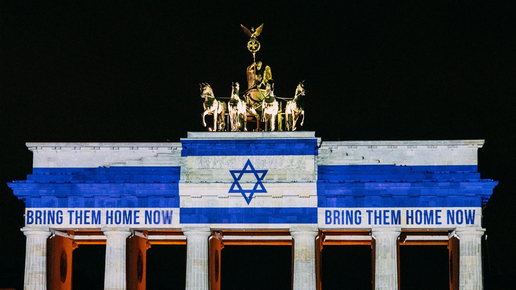 Das Brandenburger Tor, darauf ist eine israelische Fahne projeziert und es sind die Worte „Bring them home now“ zu lesen.