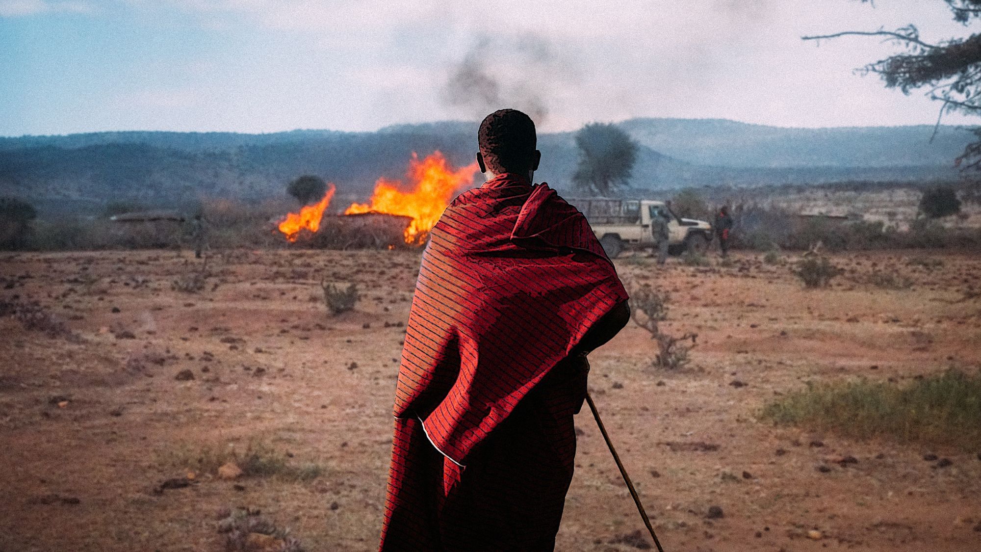 Eine Person, die in ein rotes Tuch gehüllt ist, blickt auf ein brennendes Haus. 