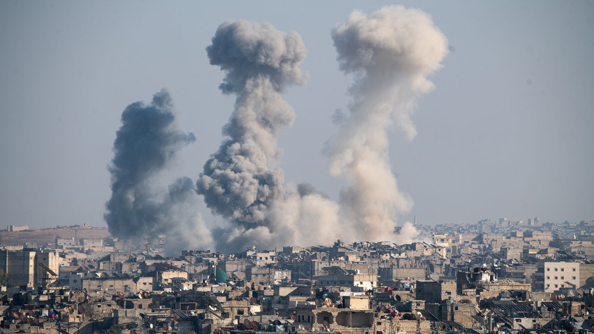 Über der Stadt Aleppo steigen drei Rauchsäulen auf.