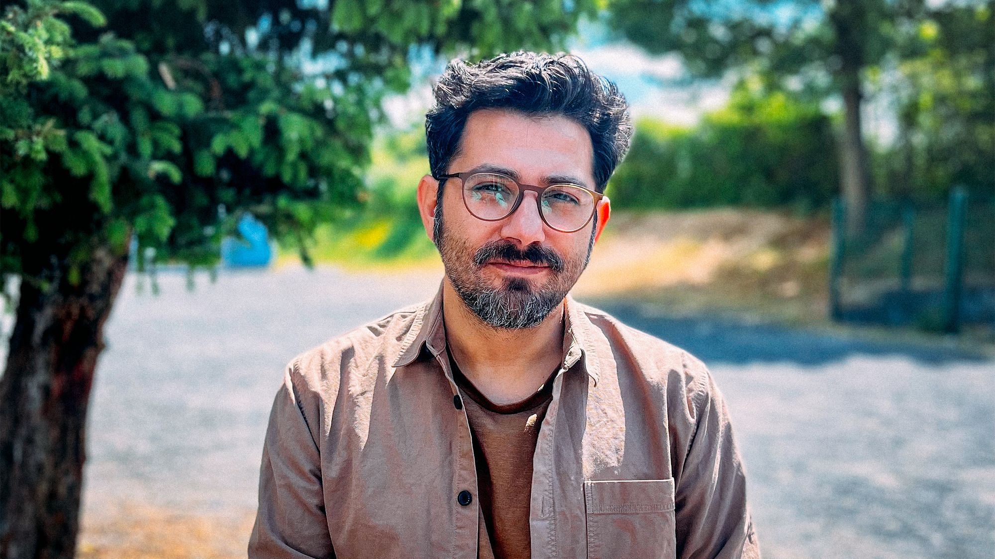 Musa blickt in die Kamera. Er trägt einen Bart und hat dunkle Haare und eine Brille.