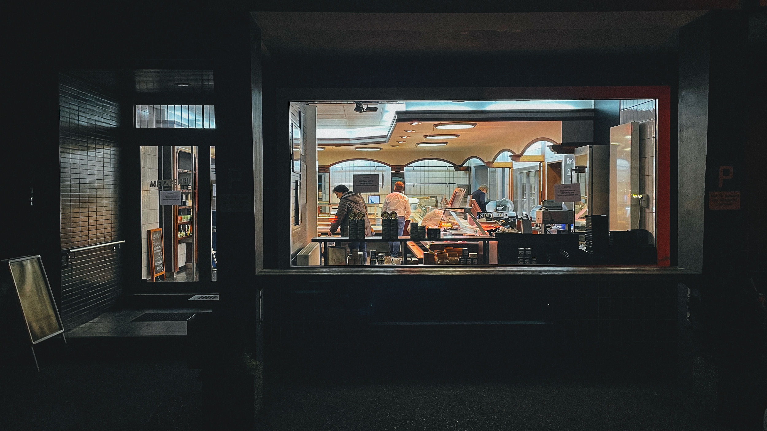 Durch ein großes Ladenfenster sieht man in eine Metzgerei hinein. Draußen ist es dunkel.