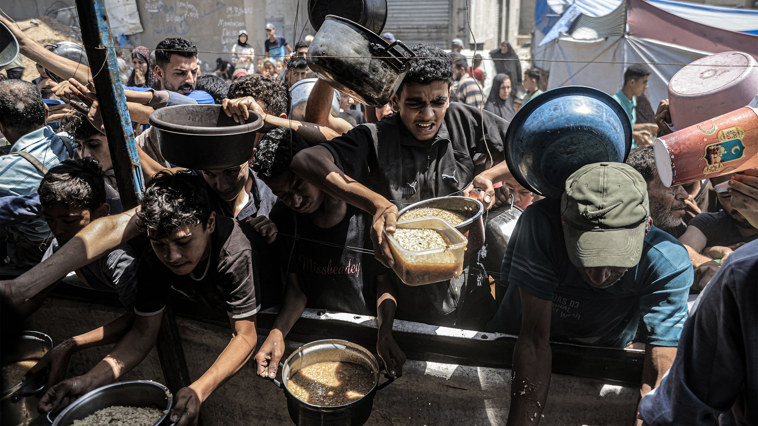 An einem Stand ringen junge Menschen um Essen. Sie tragen Töpfe und Schüsseln mit sich.