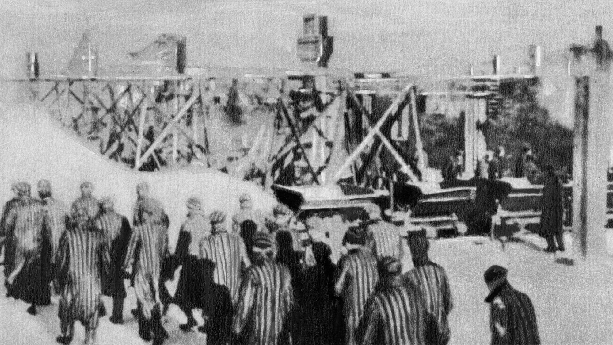 Häftlinge im Konzentrationslager gehen zur Arbeit. Im Hintergrund sieht man Holzgerüste.