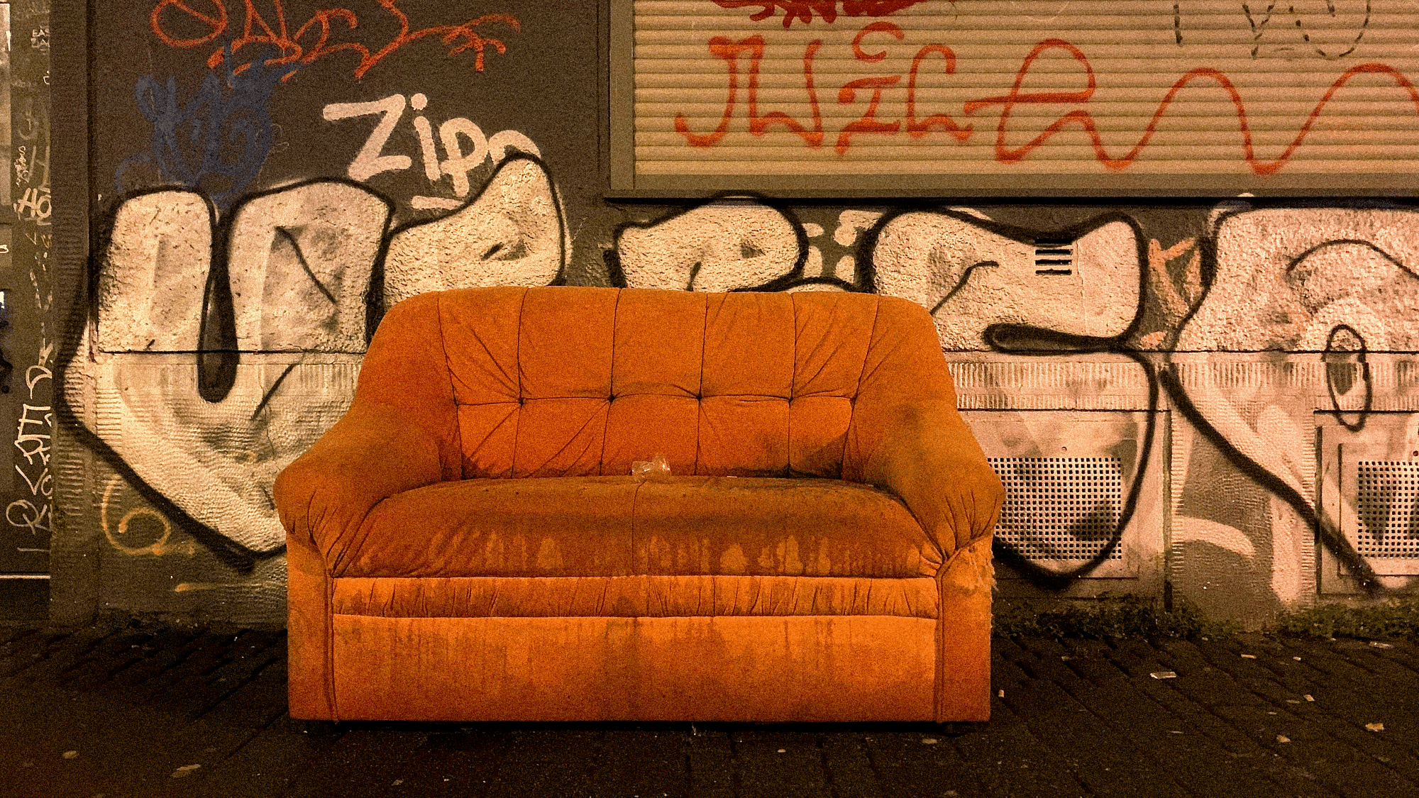 Ein heruntergekommenes Sofa steht draußen vor einer mit Grafitti vollgesprayten Wand