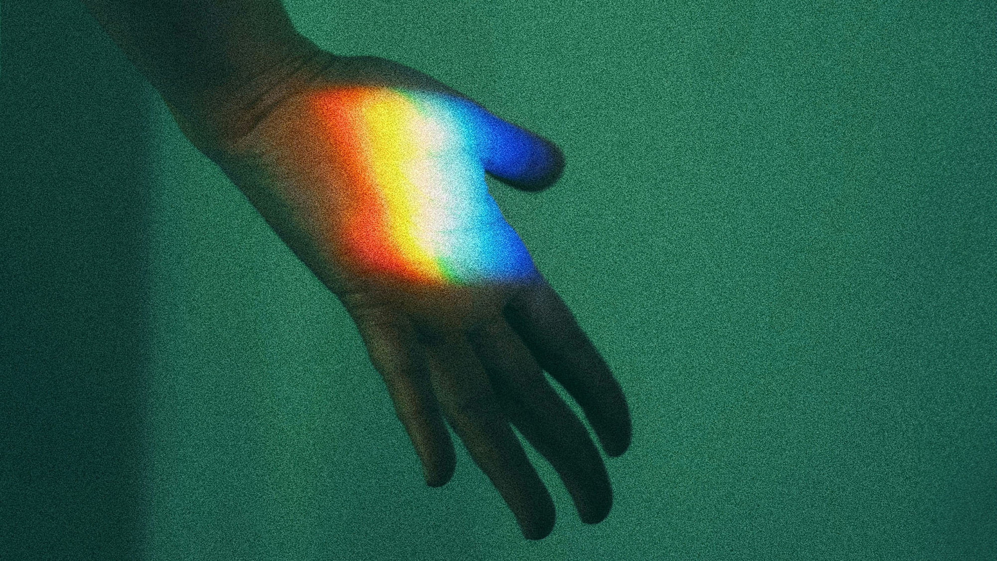 Eine Hand in einem dunklen Raum, darauf fällt das Licht eines Regenbogens