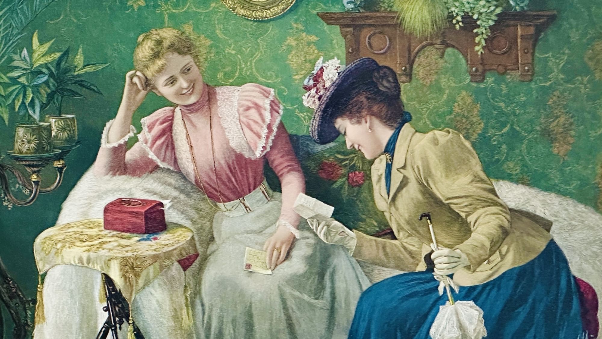 Zwei Frauen in altmodischen Kleidern sitzen vor einer grünen Wand und lesen etwas. 