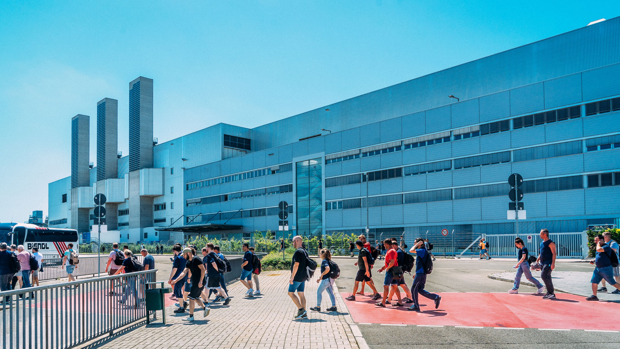 Leute laufen von dem BMW-Werk, einem großen Bau aus Metall und Glas.
