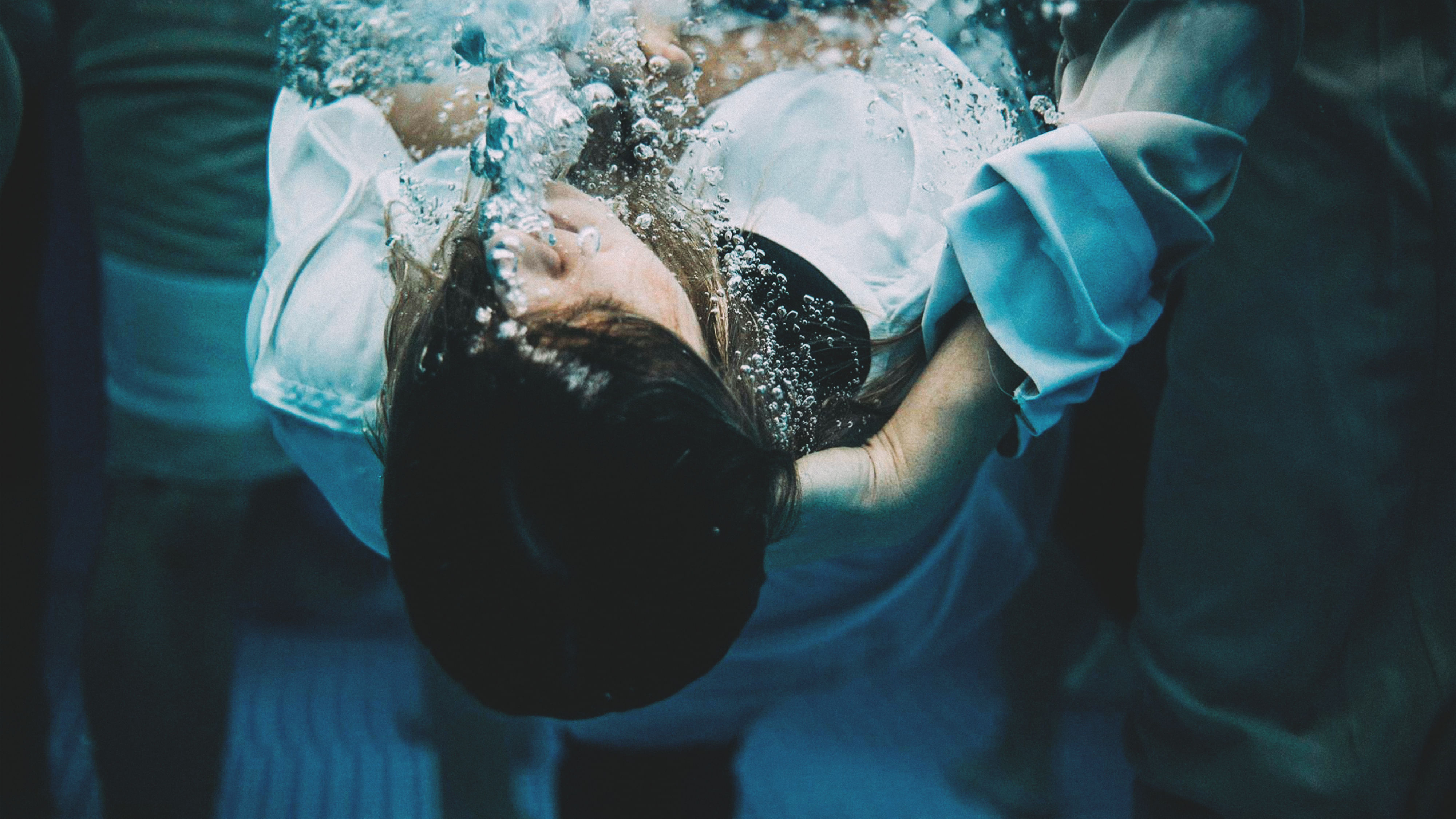 Unterwasseraufnahme: Eine Frau wird bei einer Taufe unter Wasser gedrückt. Sie trägt ein weißes Kleid. Um sie herum stehen mehrere Menschen.